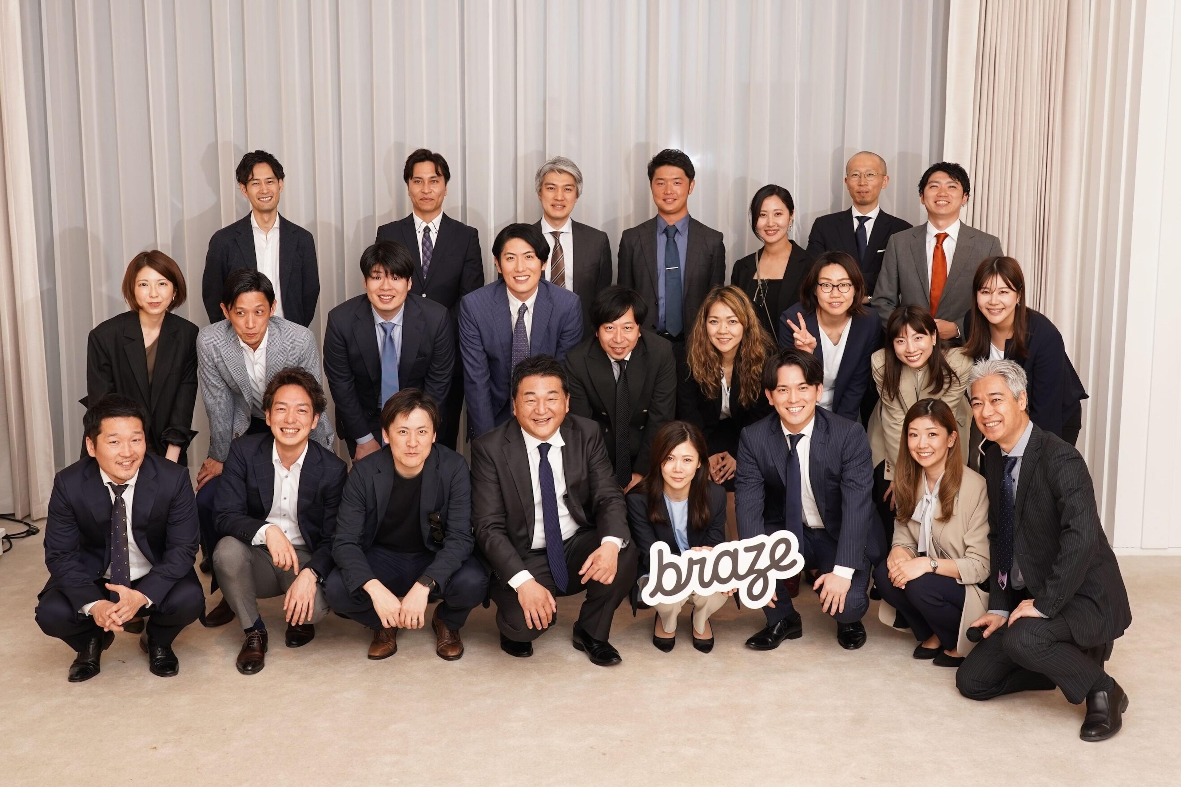 ビジネススーツを着た多くの人々が集まっているグループ写真。中央に「braze」のサインを持った人がいます。