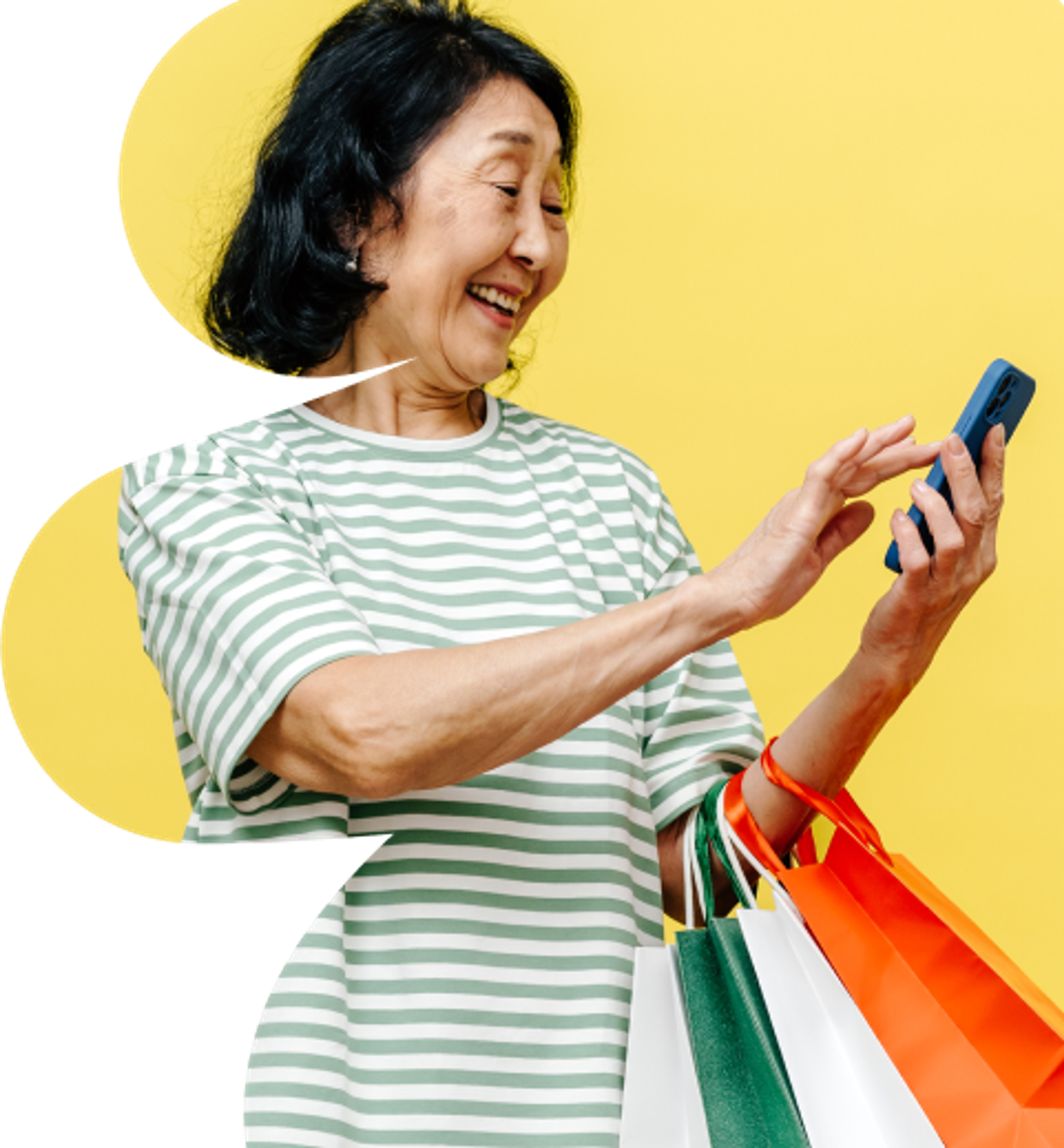 An older woman in a striped shirt smiles while holding shopping bags and looking at her phone. The background is bright yellow.