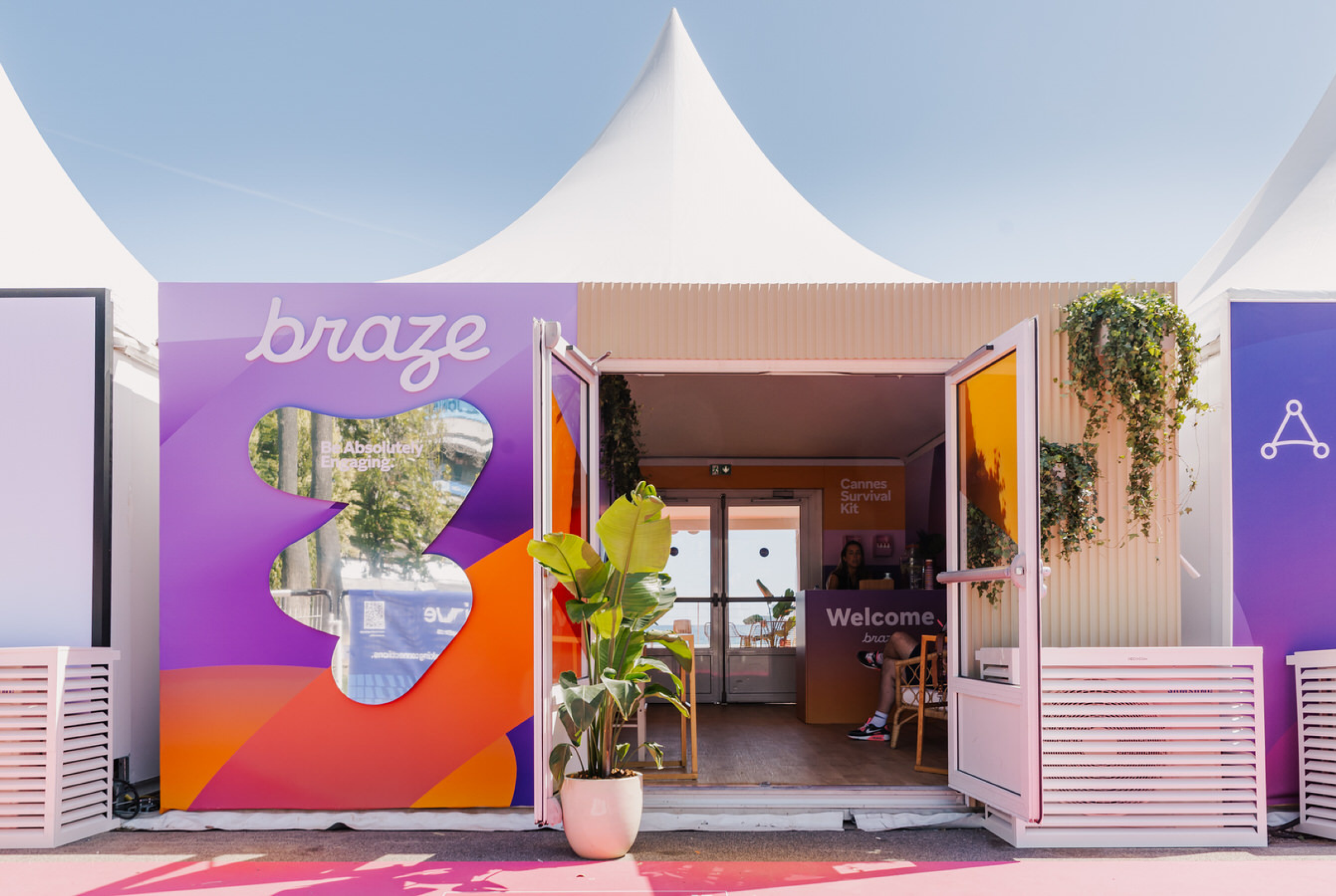 A colorful outdoor booth with the word "braze" prominently displayed. The entrance is open, revealing a welcoming interior with plants and seating.