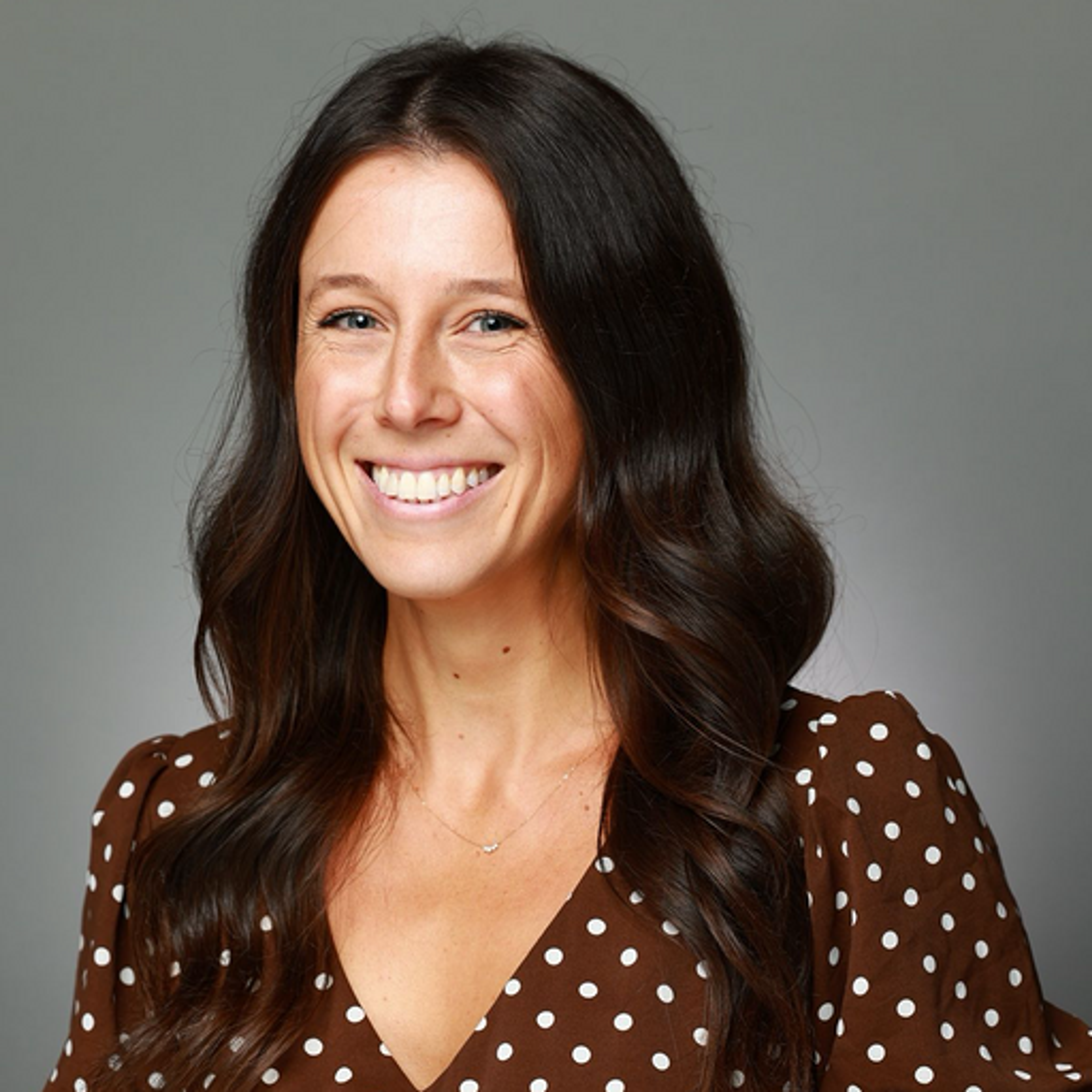 Headshot of a smiling woman with dark hair and polka dot blouse.