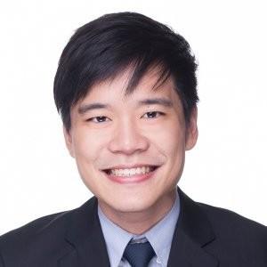A smiling young man in a suit and tie against a plain white background. He has short black hair and is looking directly at the camera.