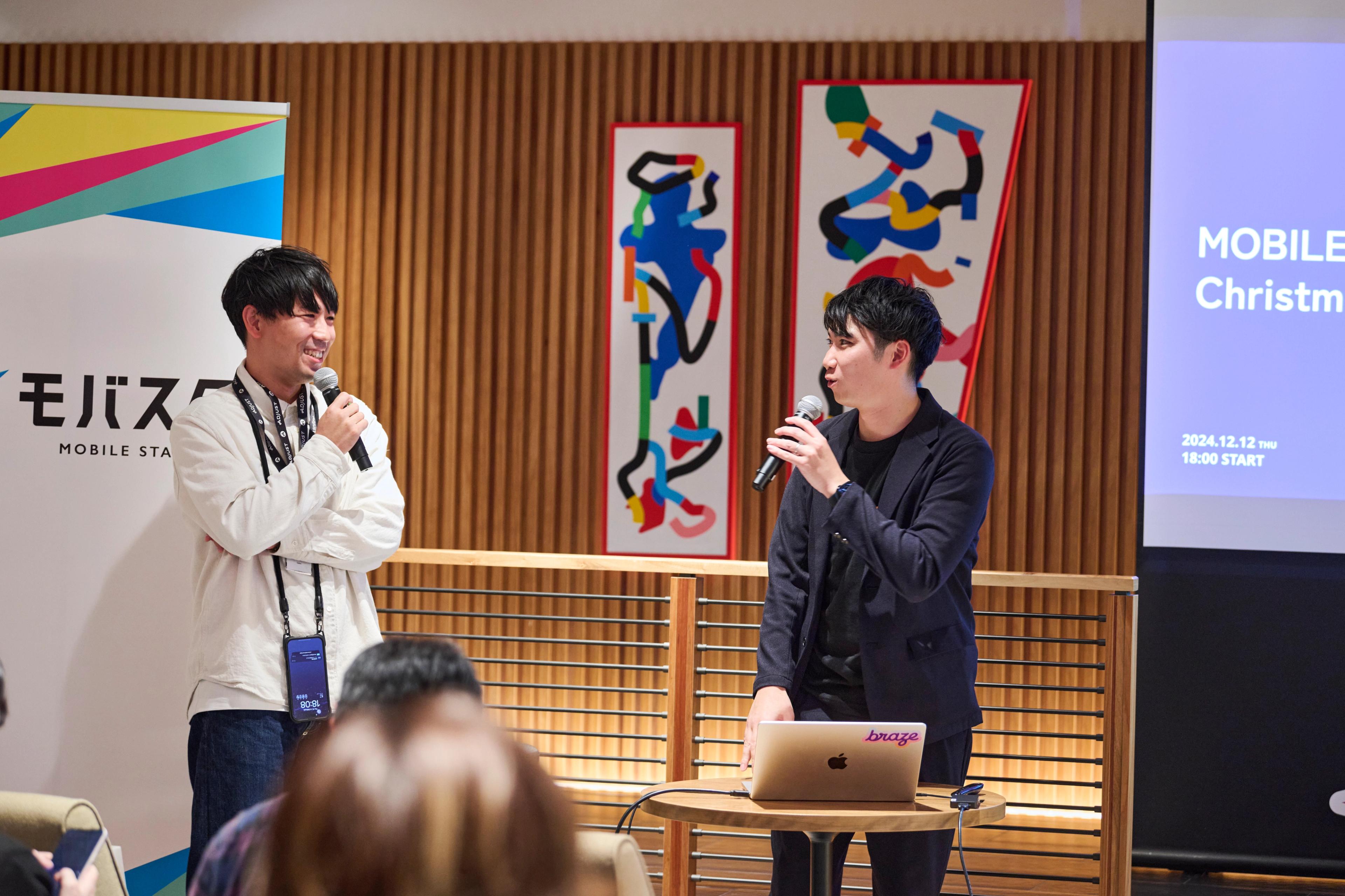 two men are standing next to each other talking into microphones in front of a crowd .