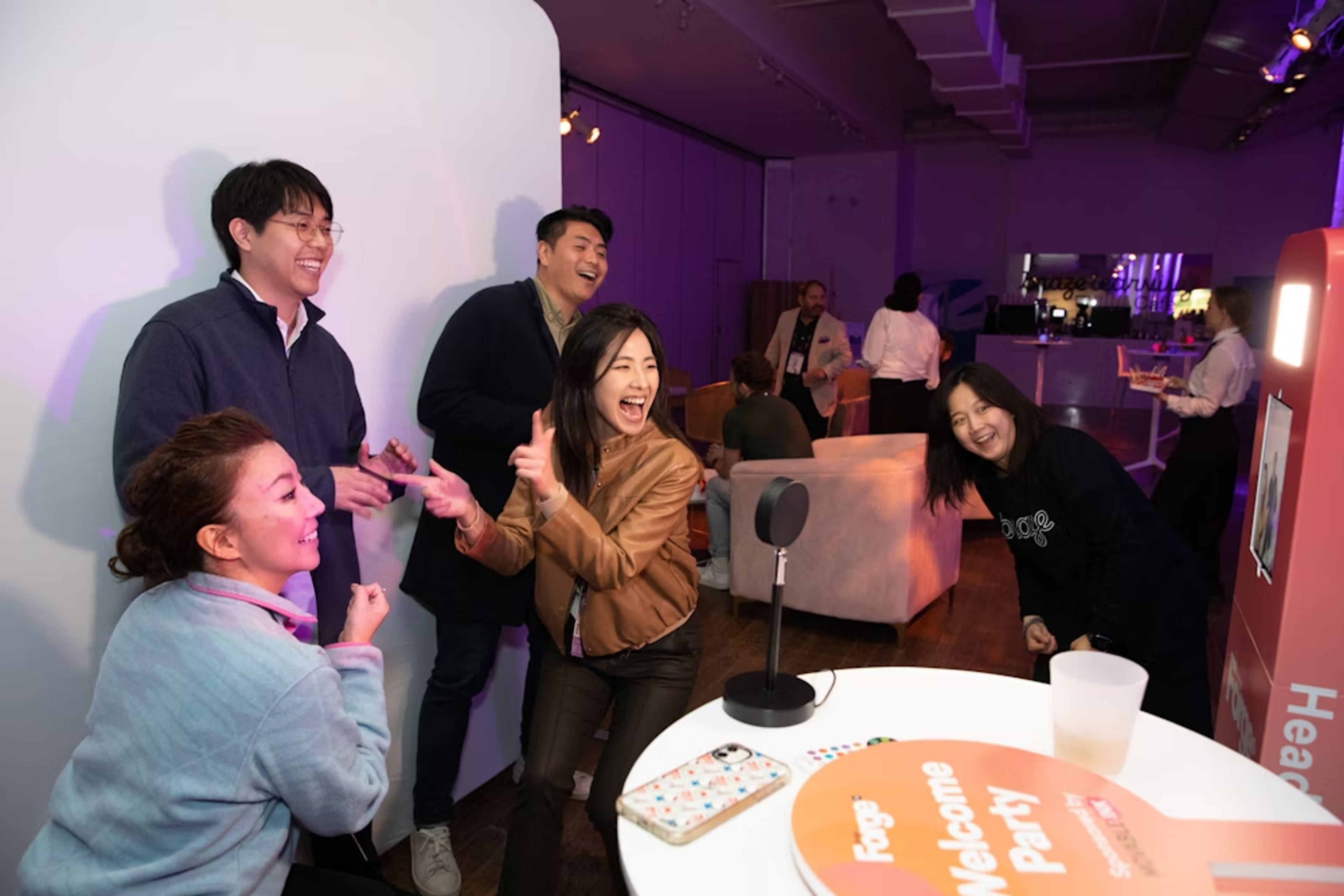 Grupo de personas riendo y posando en una fiesta, con un fondo iluminado y un micrófono en primer plano.