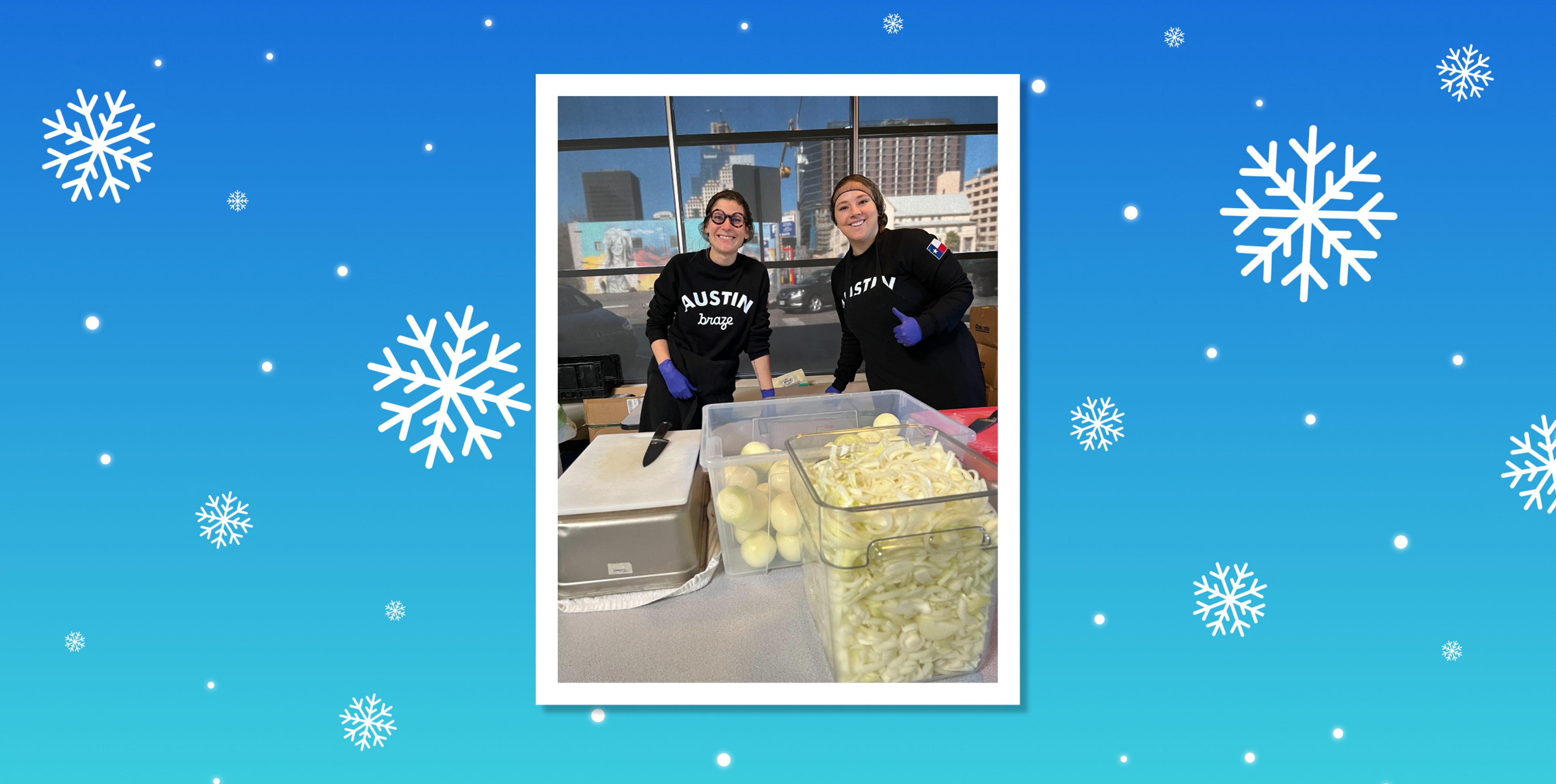 Two volunteers wearing matching black shirts smile while preparing food in a kitchen setting, with containers of sliced apples and other ingredients in front of them. The background features a winter-themed design with snowflakes.