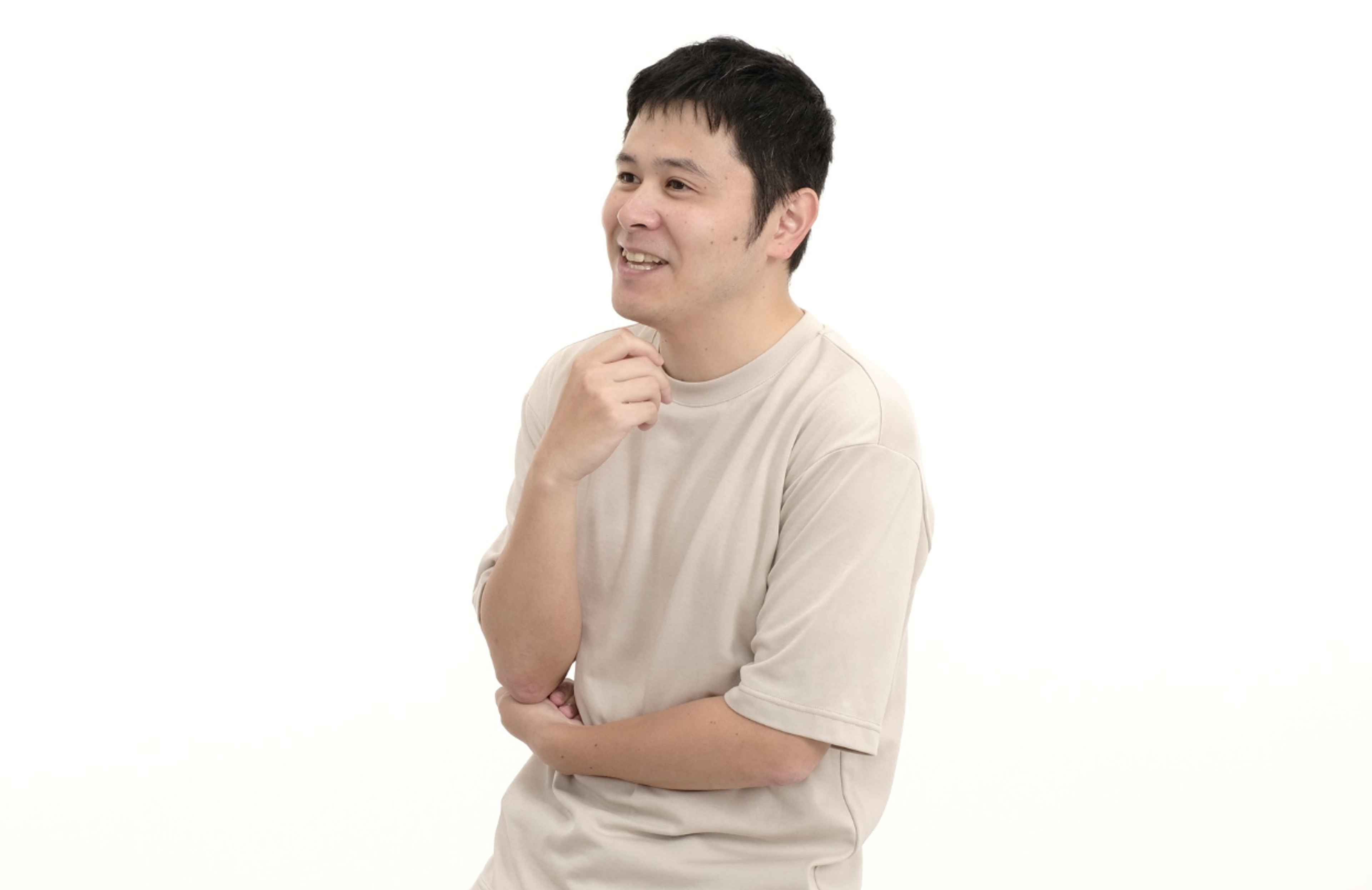 白い背景の前で微笑む男性が、手を顎に当てて考え込んでいる姿。