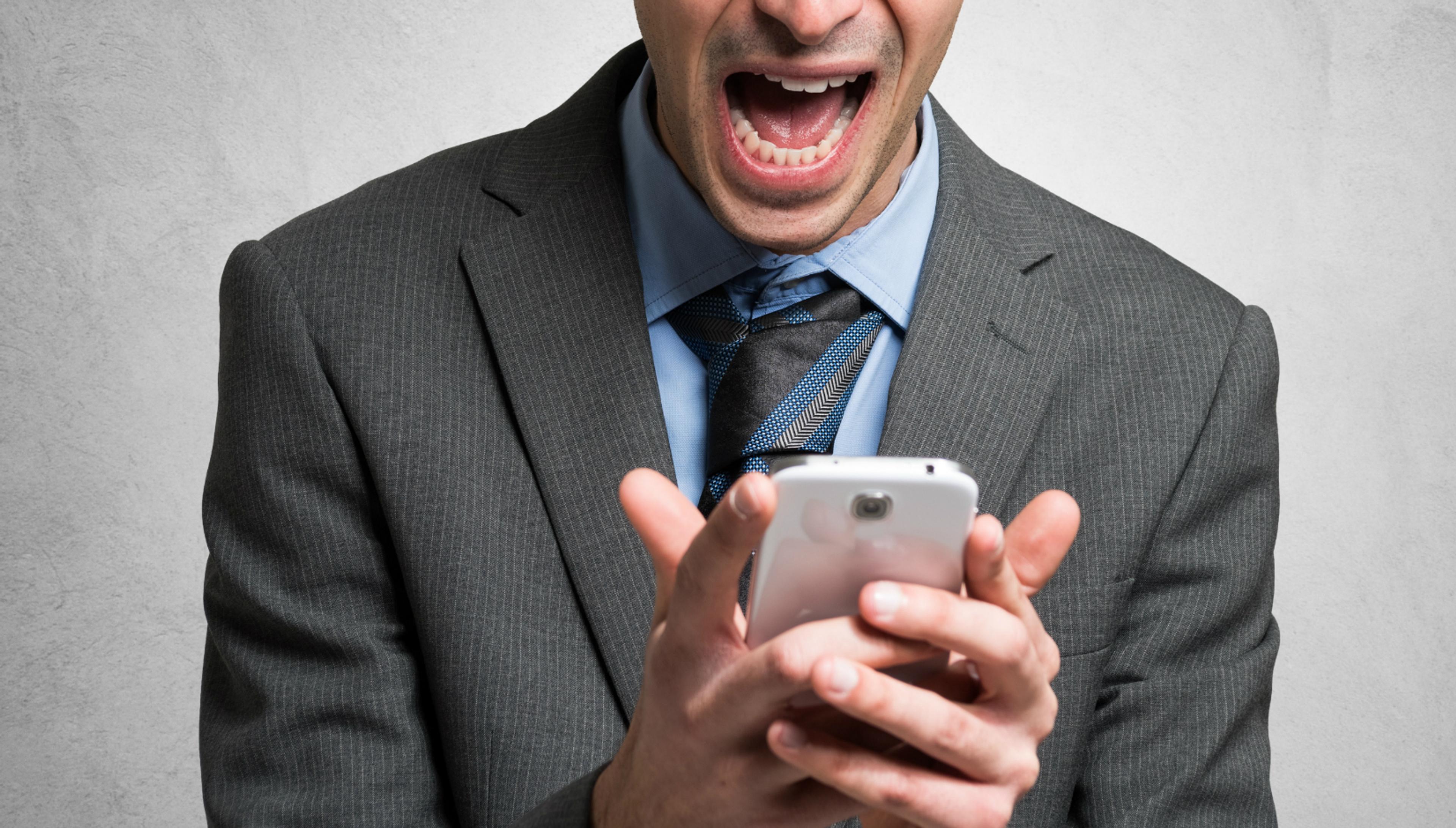 A man in a suit is shouting while looking at his smartphone. His expression conveys surprise or excitement.