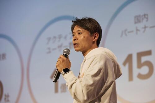 プレゼンテーション中の男性がマイクを持って話しています。背景には統計データが表示されています。