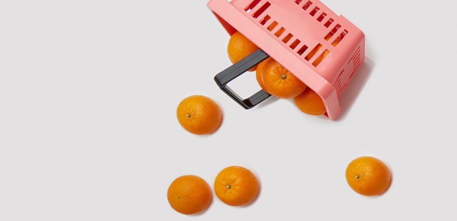 Pink shopping basket spilling oranges on a white background.