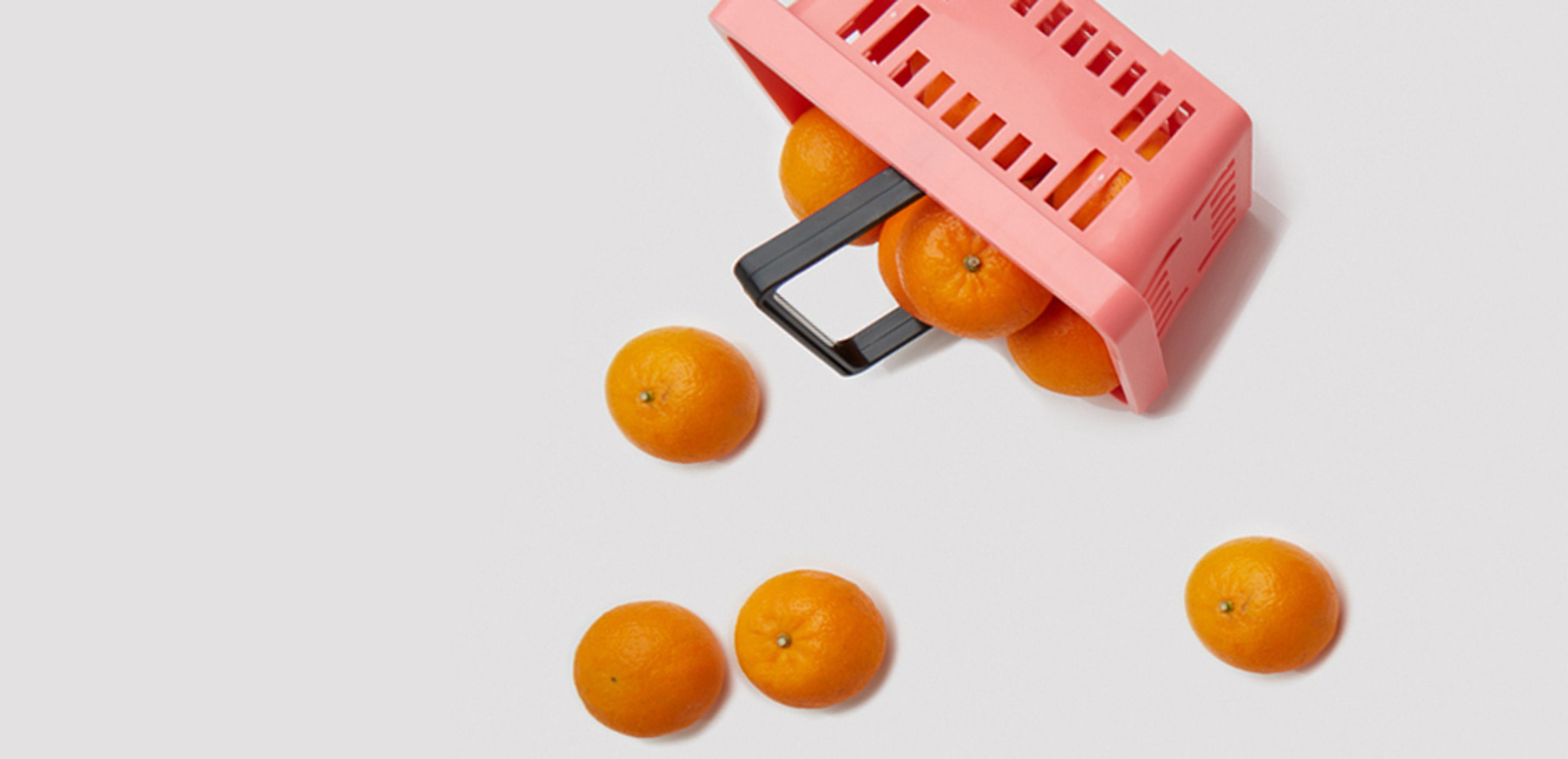 Pink shopping basket spilling oranges on a white background.