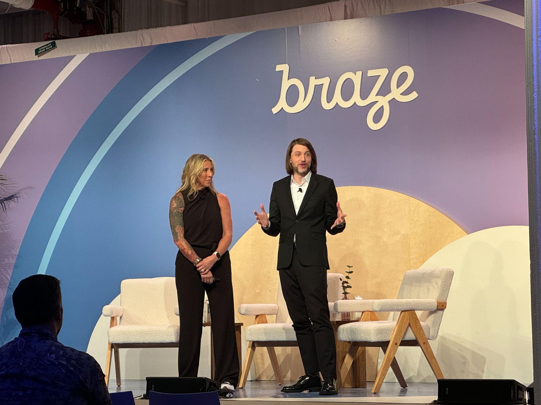ステージ上でプレゼンテーションを行う2人のスピーカーがいます。背景には「braze」のロゴがあります。