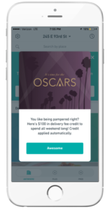 A smartphone screen displaying a promotional message for the Oscars, offering $100 in delivery credit for the weekend. The background features palm trees and a purple banner with the text "It's time for the OSCARS.