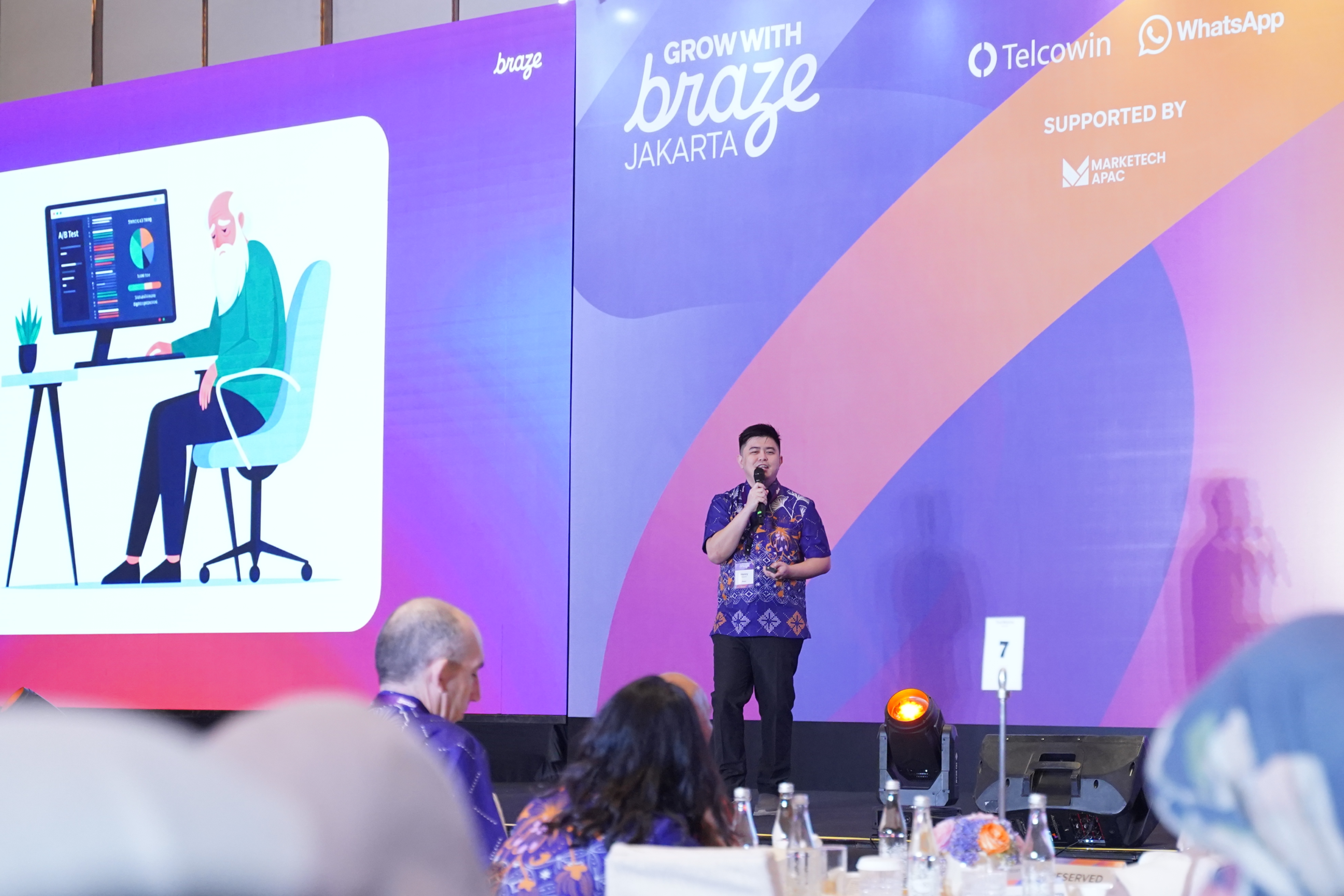 A speaker addresses attendees onstage at the Grow with Braze Jakarta event, backed by a colorful presentation screen.