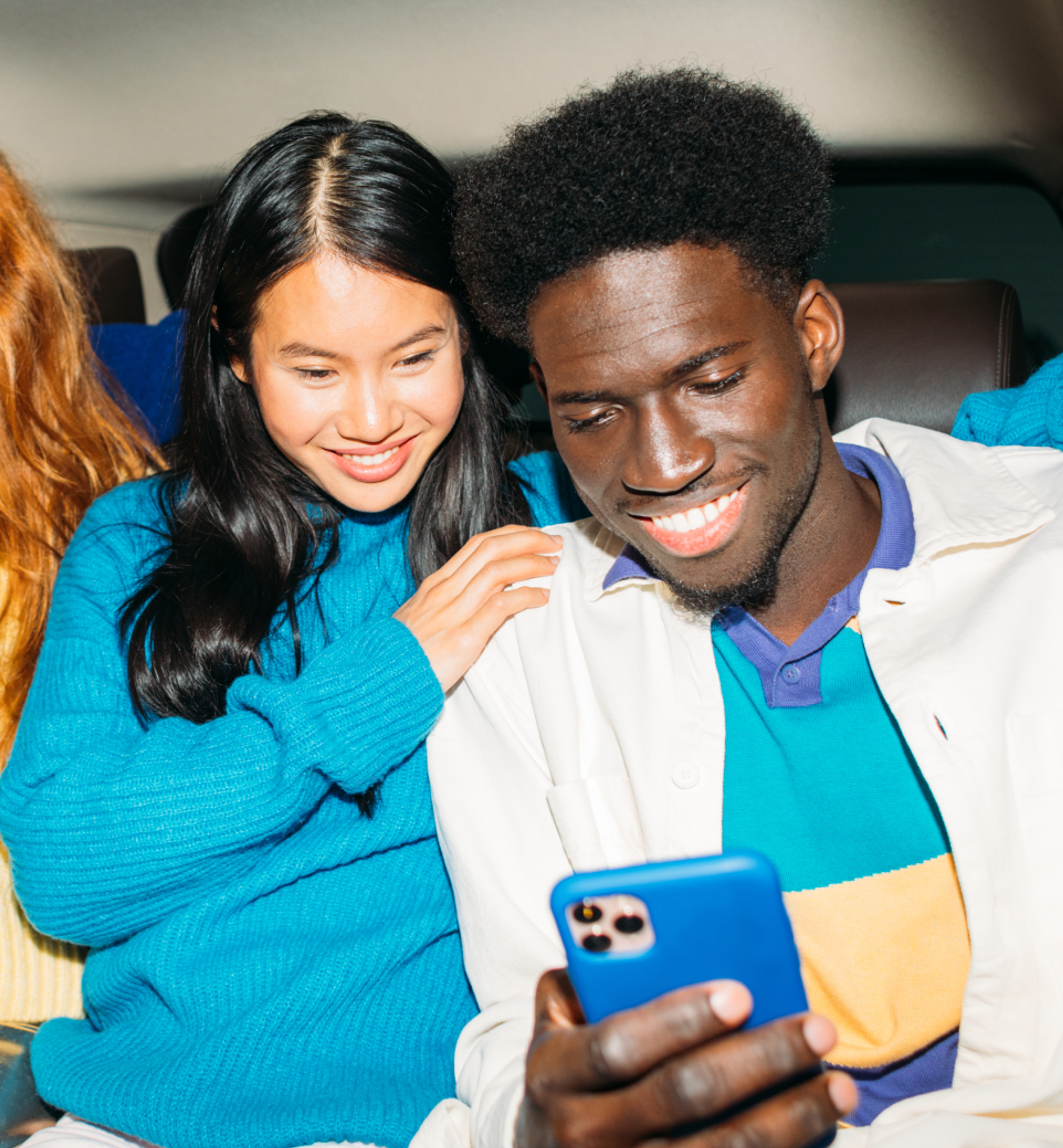 Two friends sit close together and smile as they look at something on a smartphone.