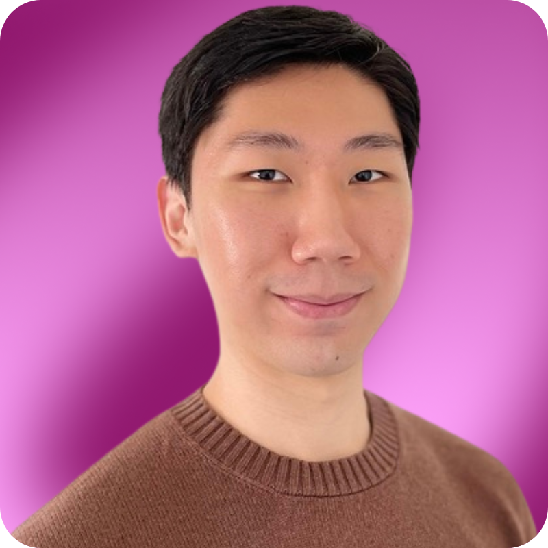 A young man with short black hair is smiling, wearing a brown sweater against a light background.