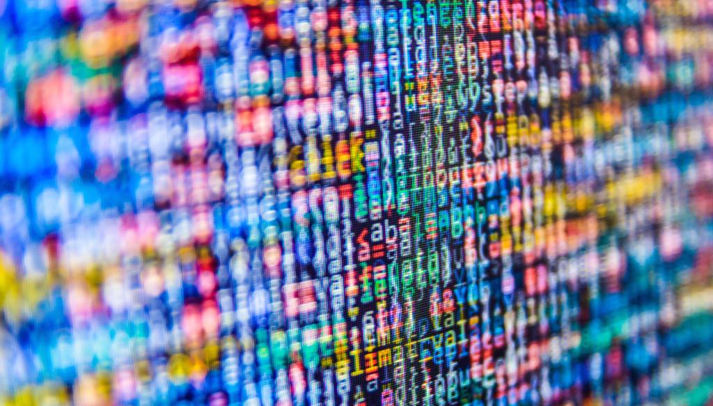 A close-up of colorful, abstract digital code displayed on a screen, featuring a mix of letters and numbers. The image has a blurred effect, emphasizing the vibrant colors.