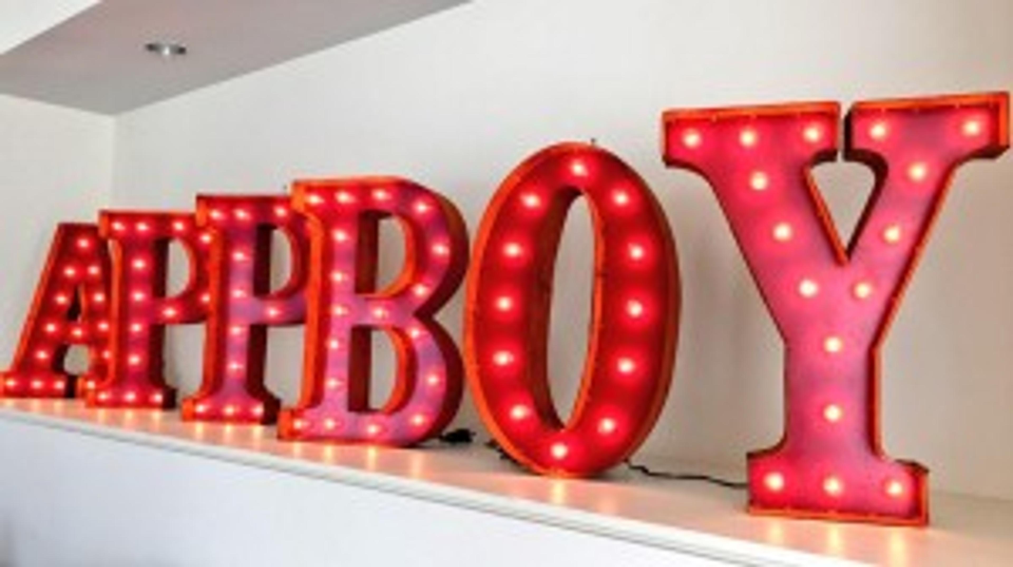 Brightly lit marquee letters spelling "APPBOY" on a shelf. The letters are pink with white bulbs.