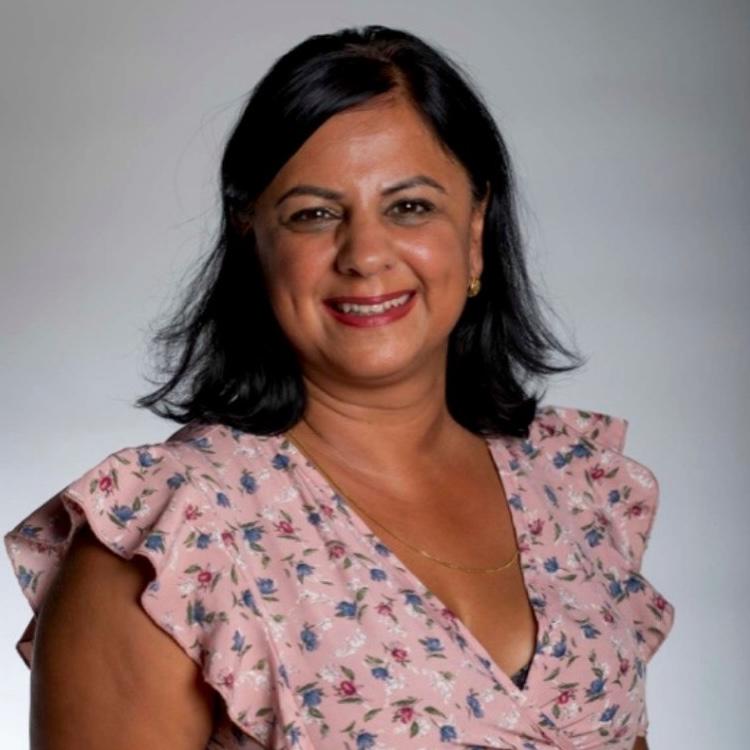 A woman with dark hair wearing a floral dress smiles at the camera. The background is a soft gray.