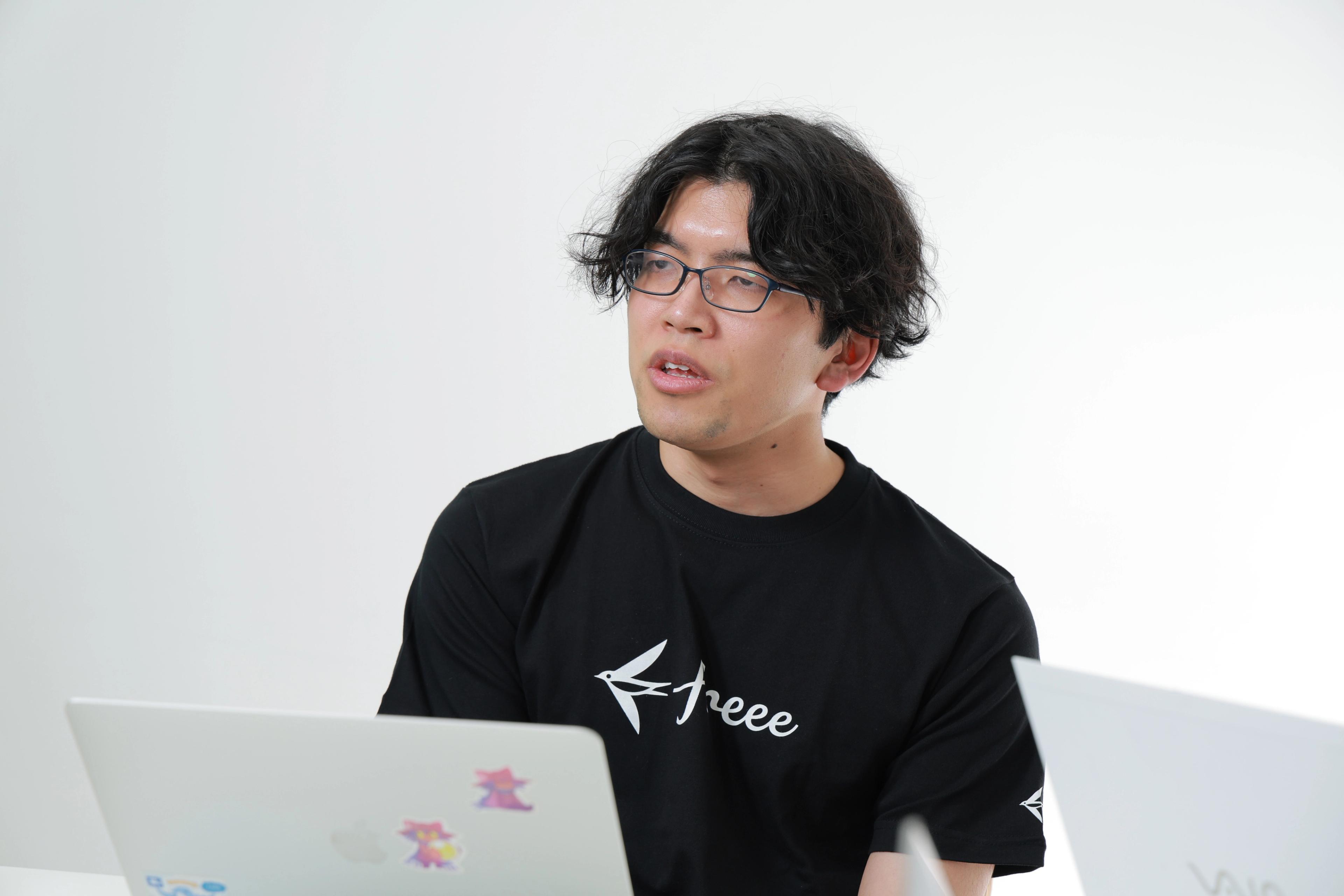 ビジネス基盤本部 IT企画推進部 MOps基盤チーム 萬田氏がPCの前でインタビューを受け、freeeのロゴ黒Tシャツを着ている