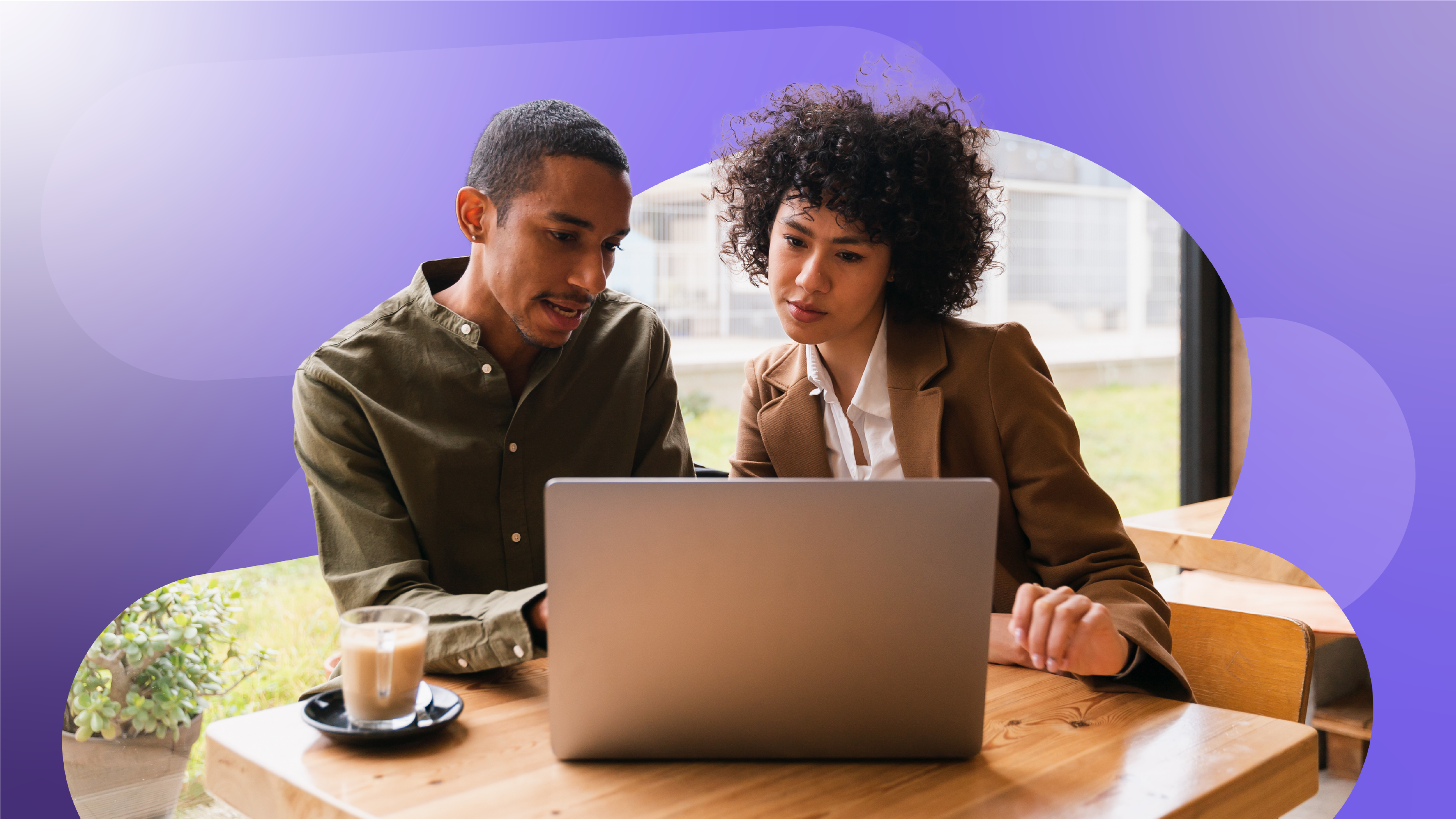 Two people sit at a table looking at an open laptop