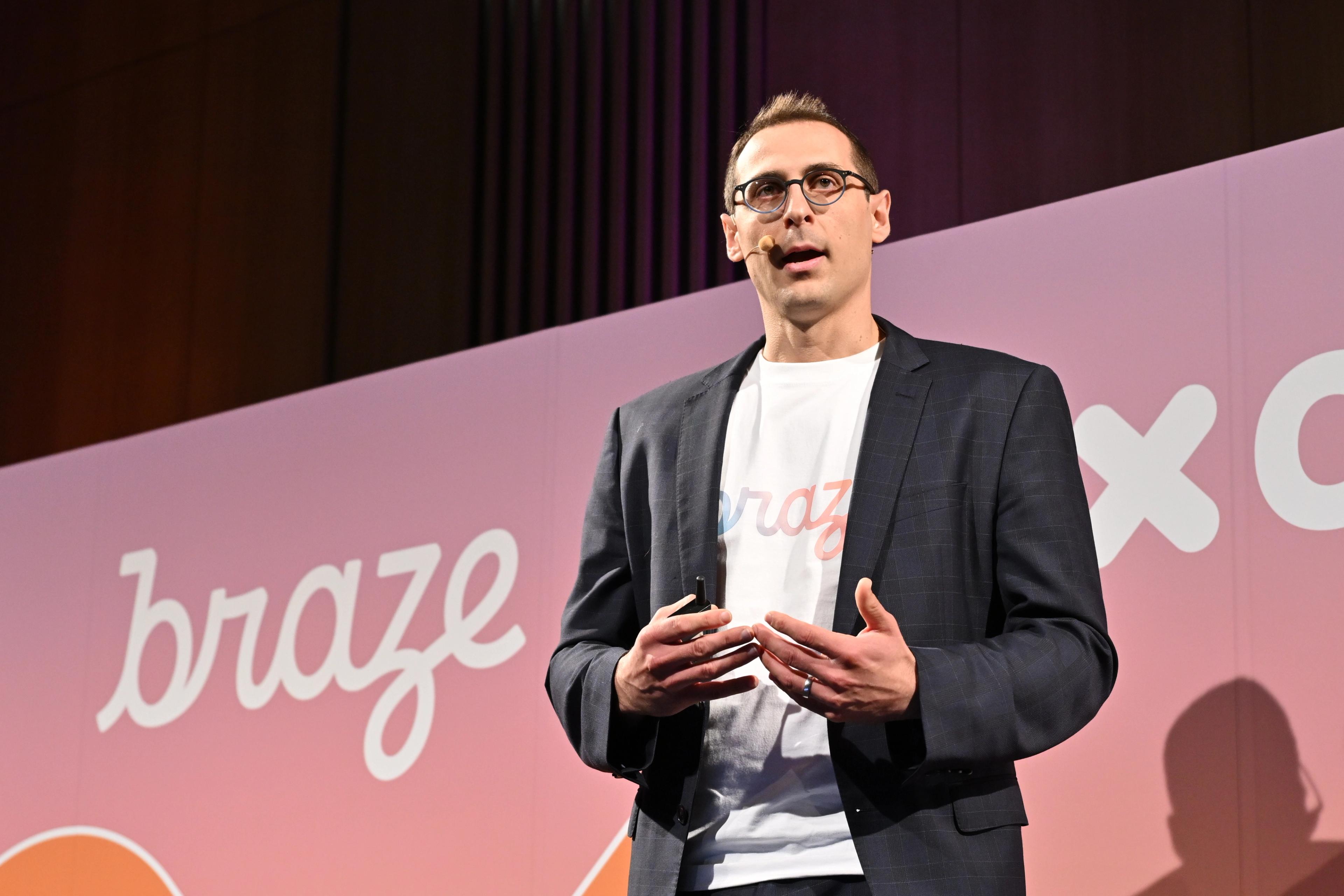 男性が「braze」のロゴがある背景の前でプレゼンテーションを行っています。彼はスーツを着ており、話している様子です。
