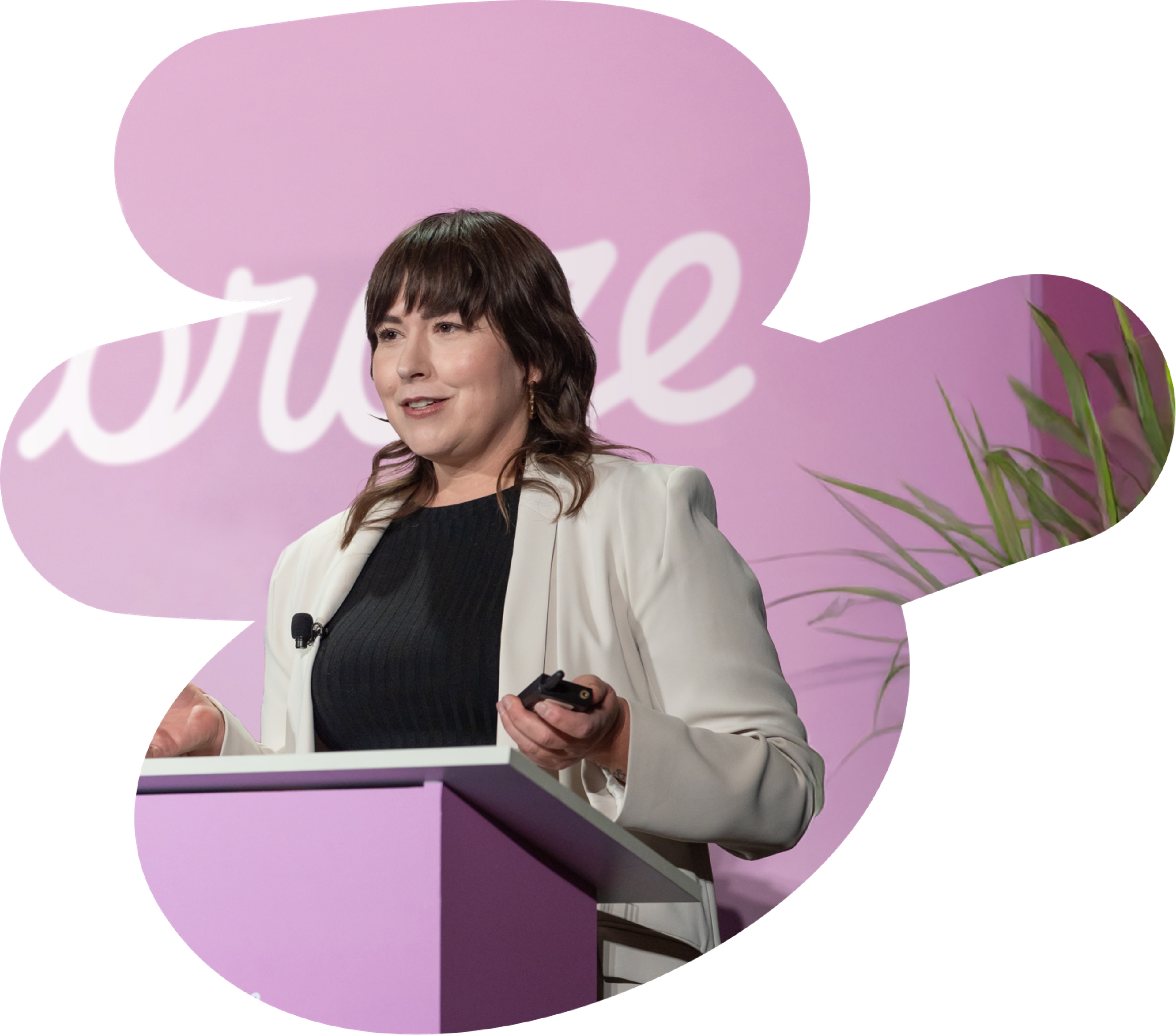 A woman in a white blazer speaks at a purple podium, holding a clicker, against a pink background with the word "embrace."