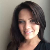 A woman with long, dark hair smiles at the camera. She has blue eyes and is wearing a black shirt.