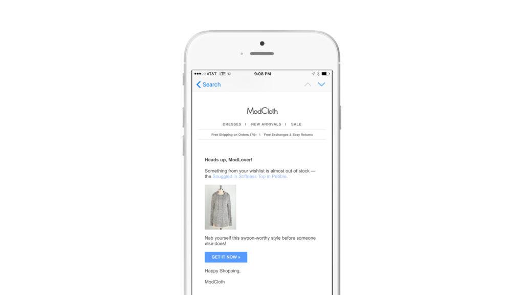 A mobile phone screen displaying an email from ModCloth about an item in the user's cart that is almost out of stock. The email includes a photo of a gray sweater and a "Get It Now" button.