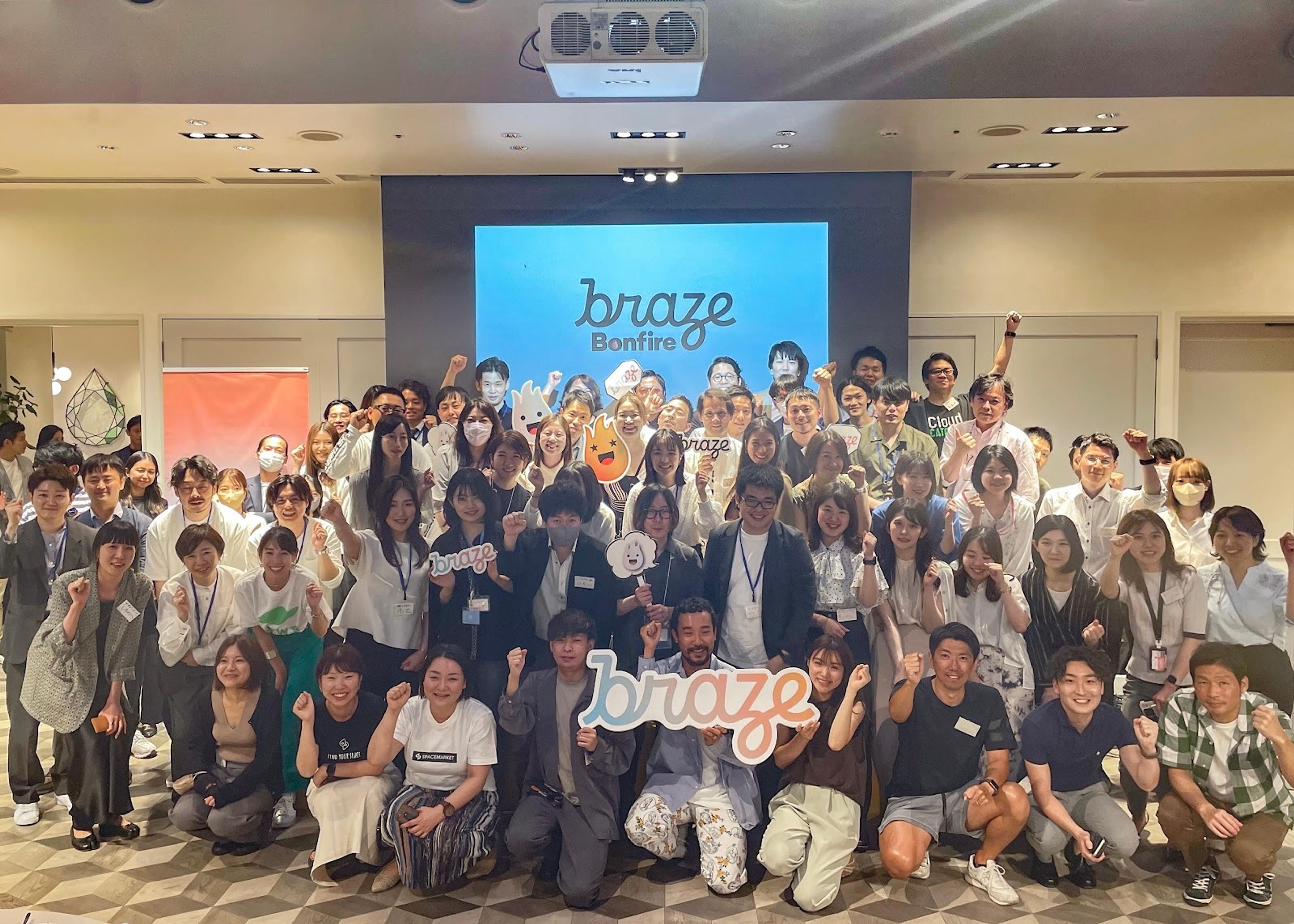 多くの人々が集まっているイベントの写真。参加者は「braze」のロゴを持ってポーズをとっています。