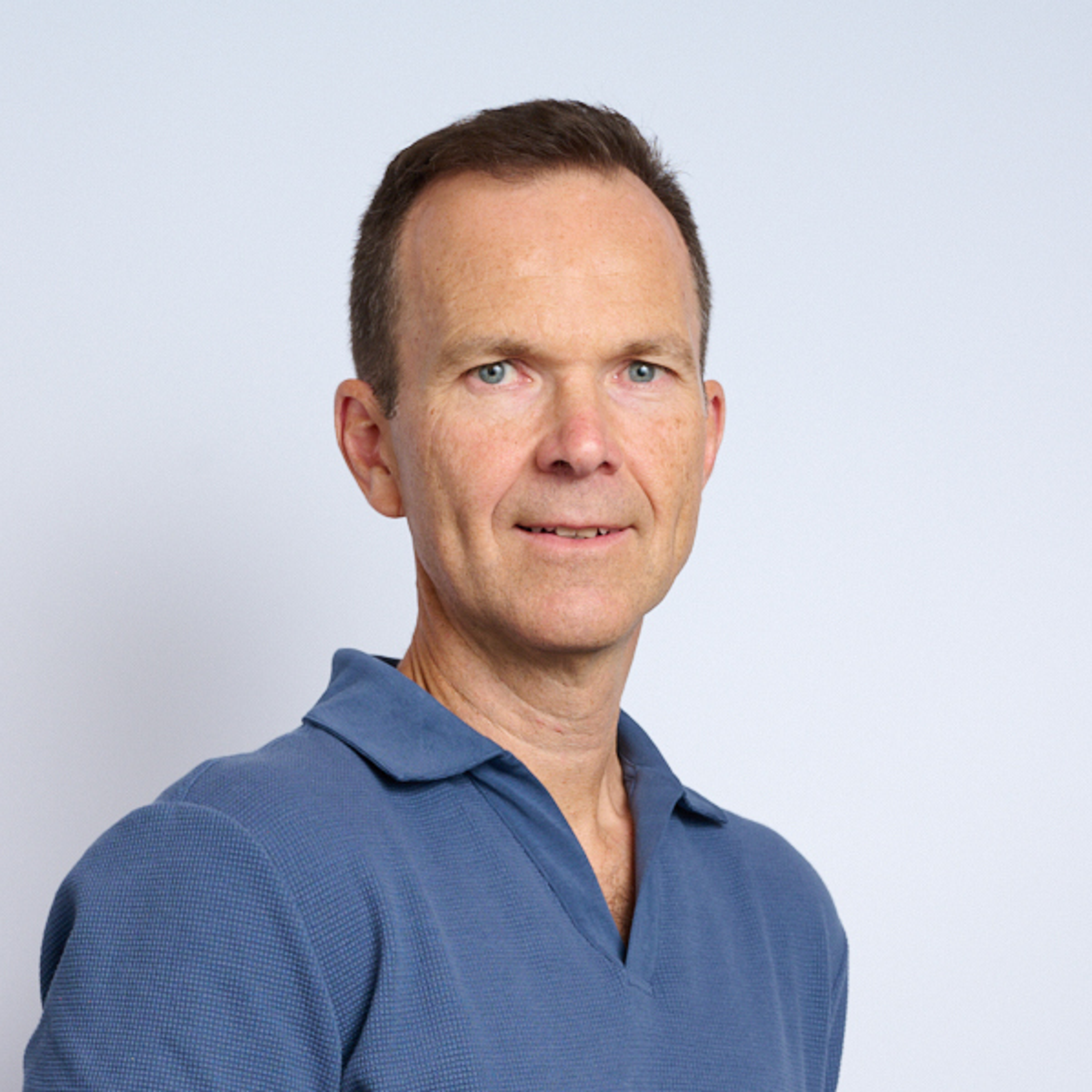 Portrait of a middle-aged man in a blue collared shirt, looking at the camera against a plain light background.
