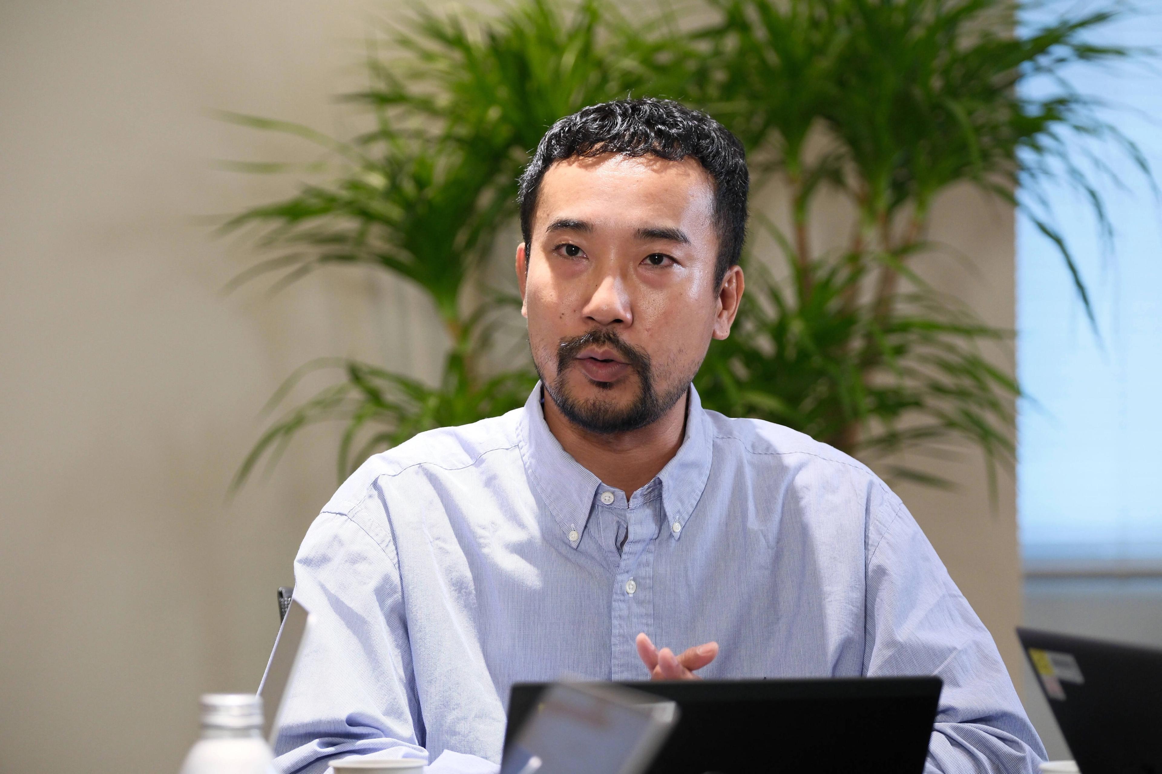 男性が会議で話している様子。背景には観葉植物があります。