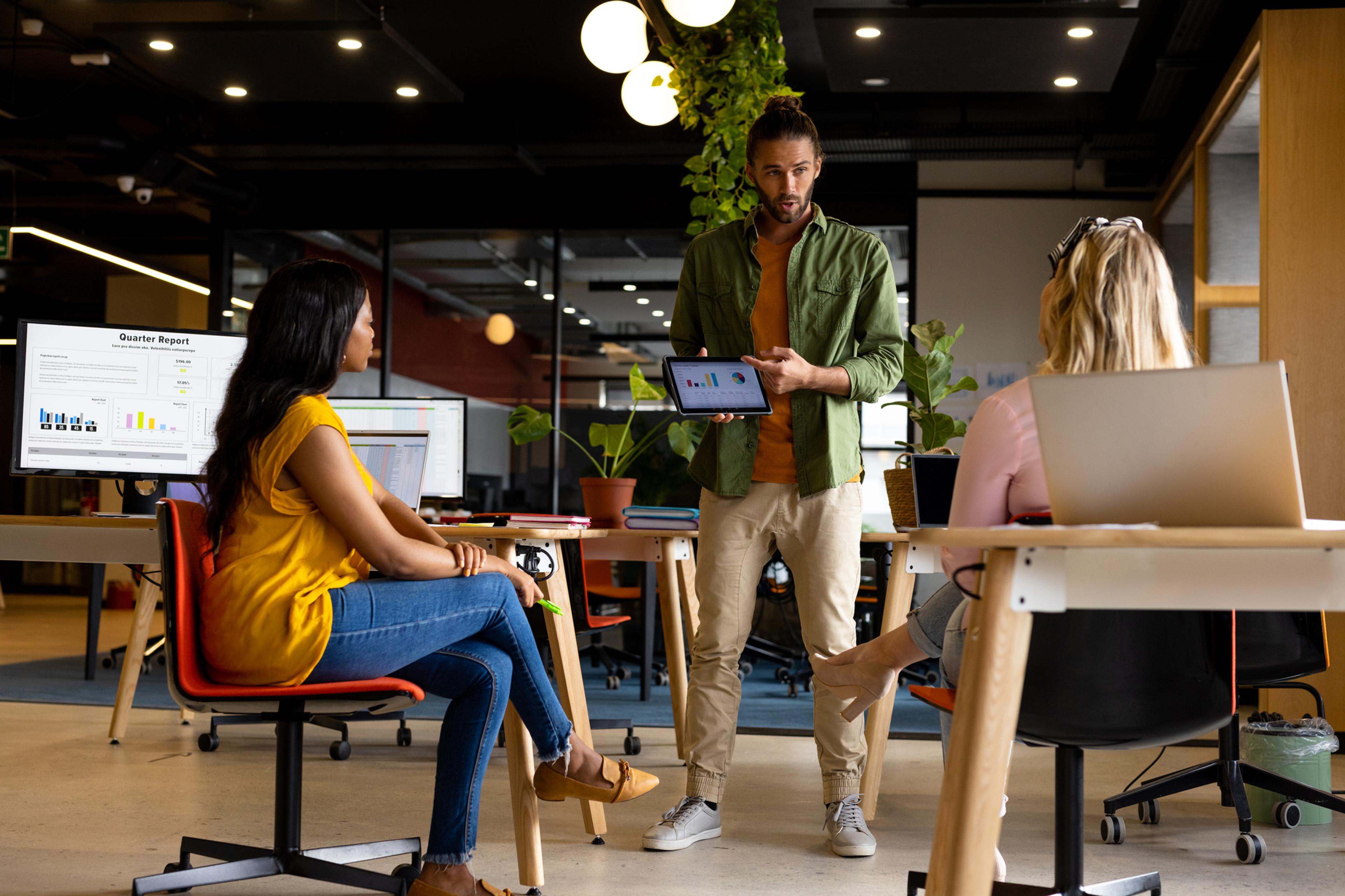 a man is holding a tablet in front of a group of people in an office .