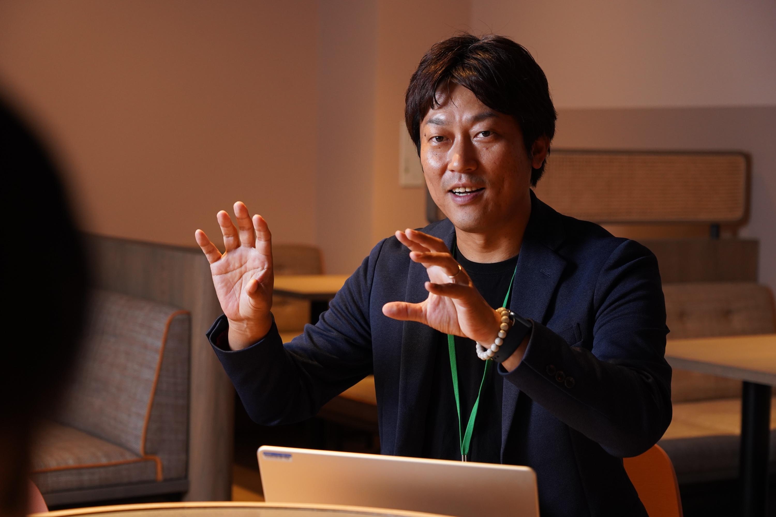 男性がラップトップの前で話している様子。手を使って説明をしている。