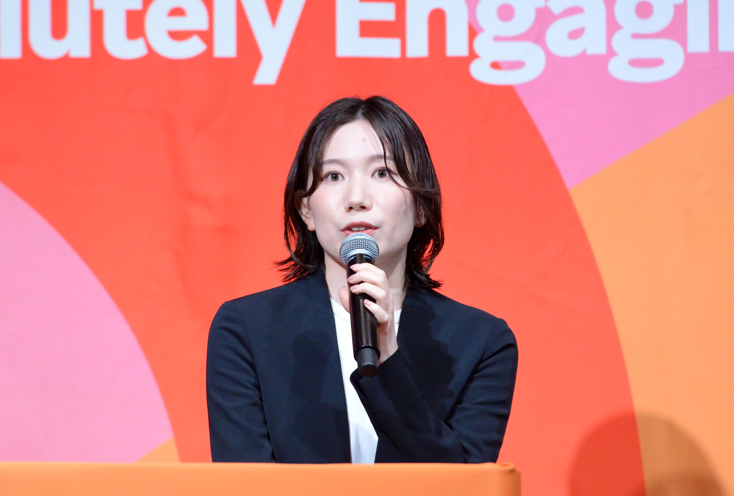 a woman in a suit is holding a microphone in front of a red background .