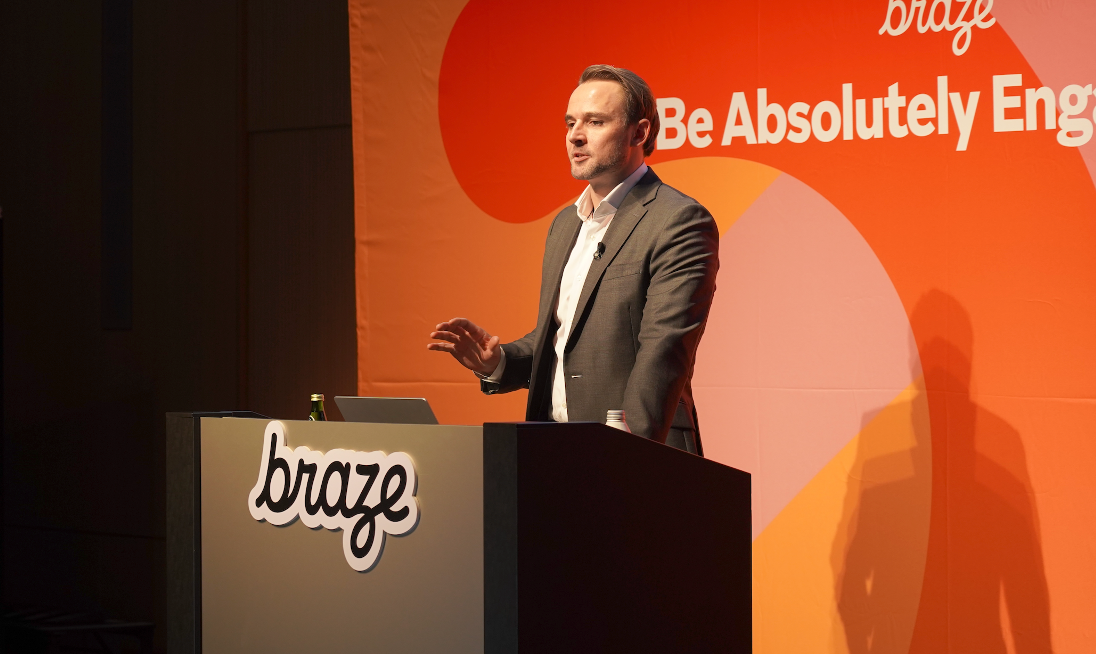 男性がプレゼンテーションを行っている様子。背景には「Be Absolutely Engaged」というメッセージが表示されている。