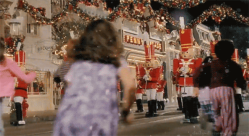 Children running towards a festive parade featuring toy soldiers and holiday decorations. The scene is lively and filled with excitement.