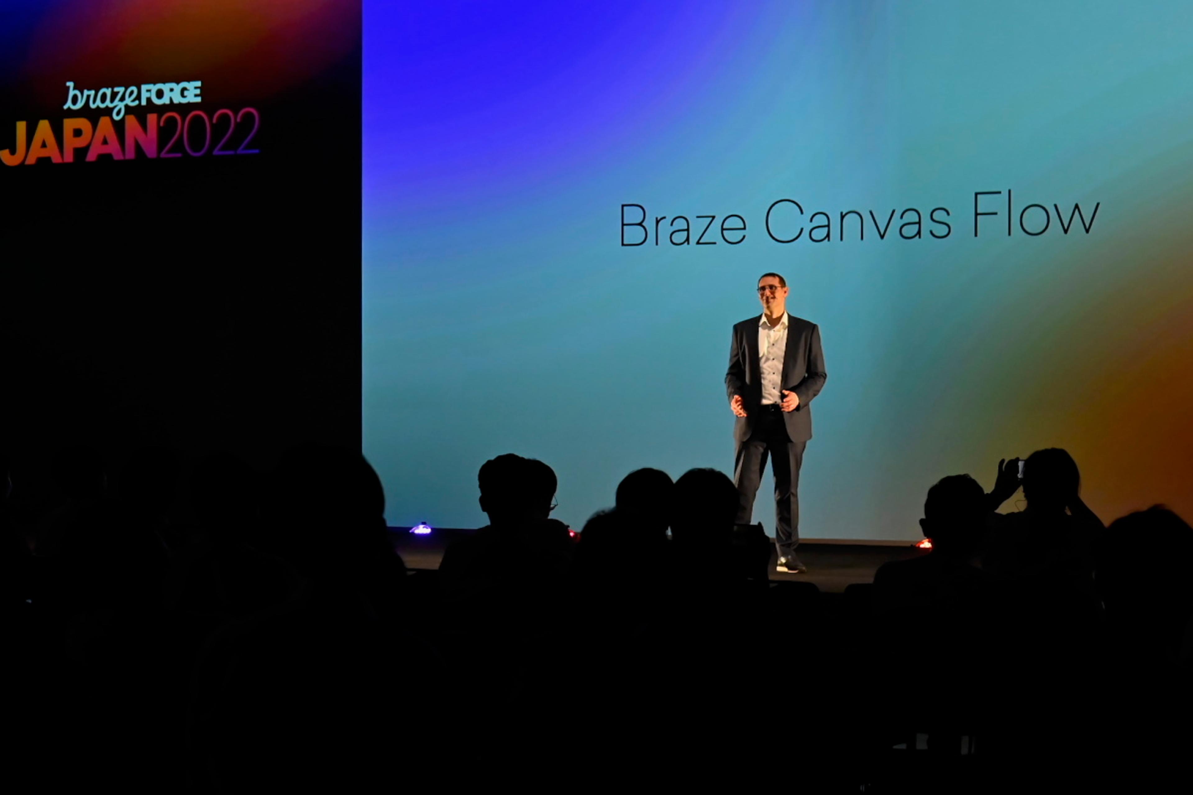 ブラゼフォースジャパン2022のステージでプレゼンテーションを行う男性。背景には「Braze Canvas Flow」と表示されている。