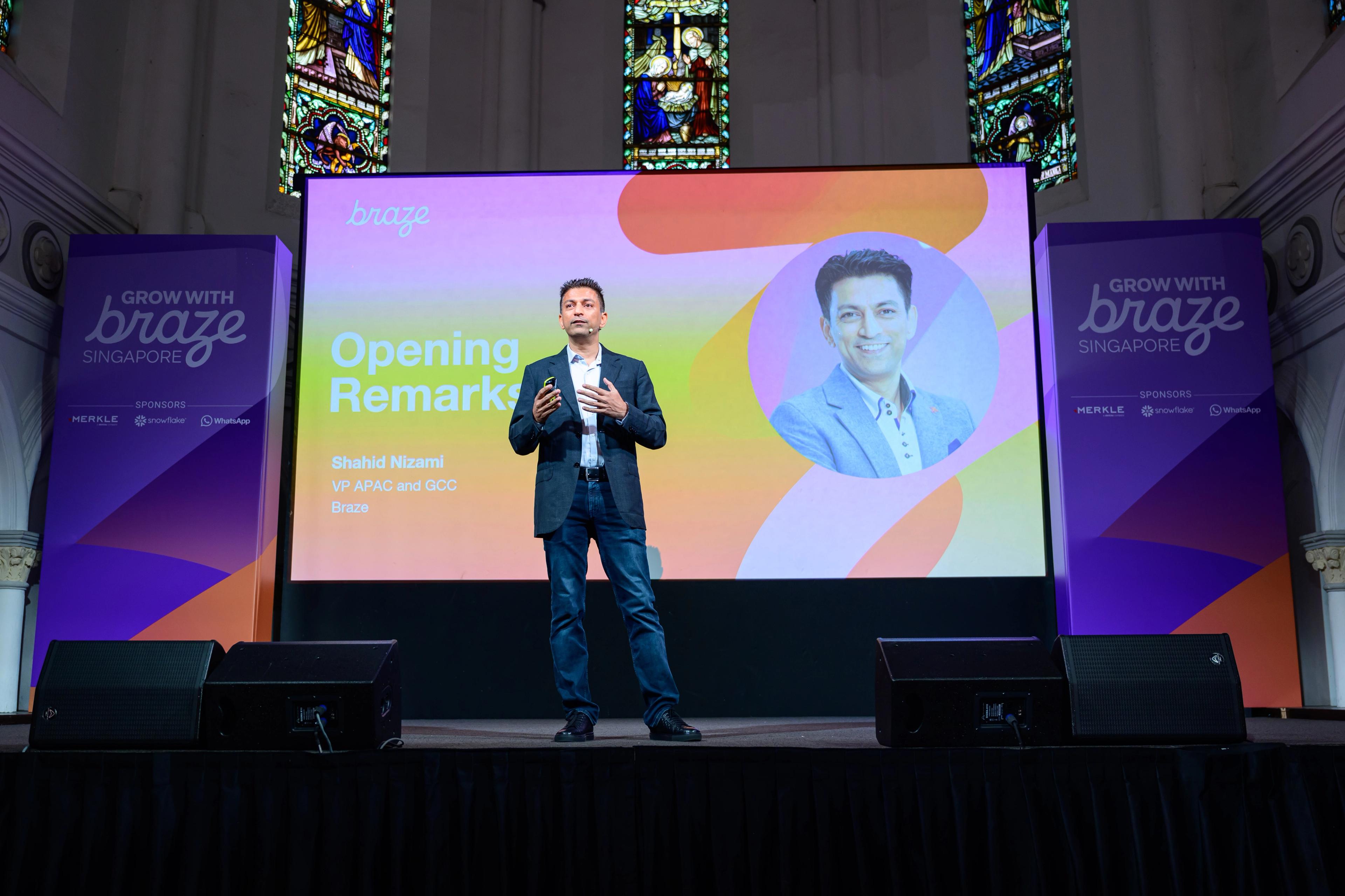 a man is standing on a stage giving a speech in front of a large screen .