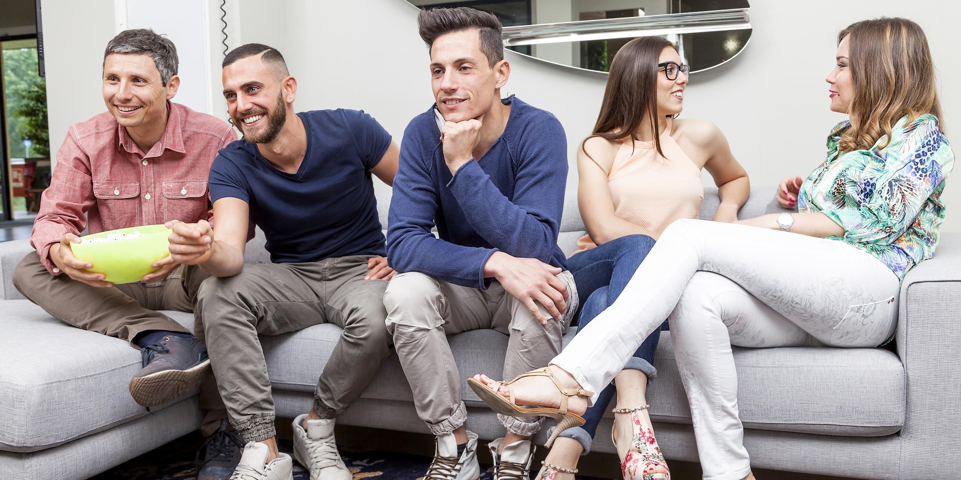 Five people sitting on a couch, engaged in conversation. They appear relaxed and are casually dressed.