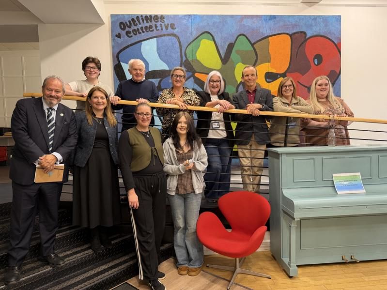 Daniel Szor with young people and colleagues on a staircase in front of an Outlines Collective mural