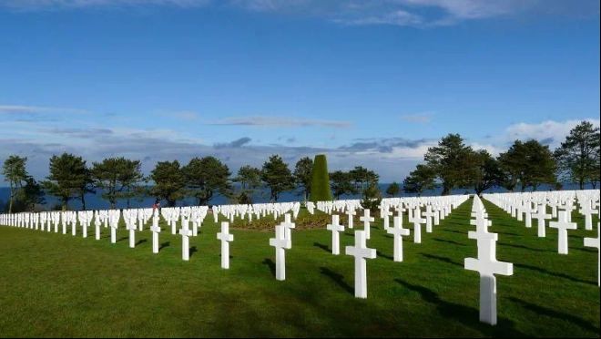 Rows of white crosses at the Normandy American Cemetery, with the sea beyond the trees