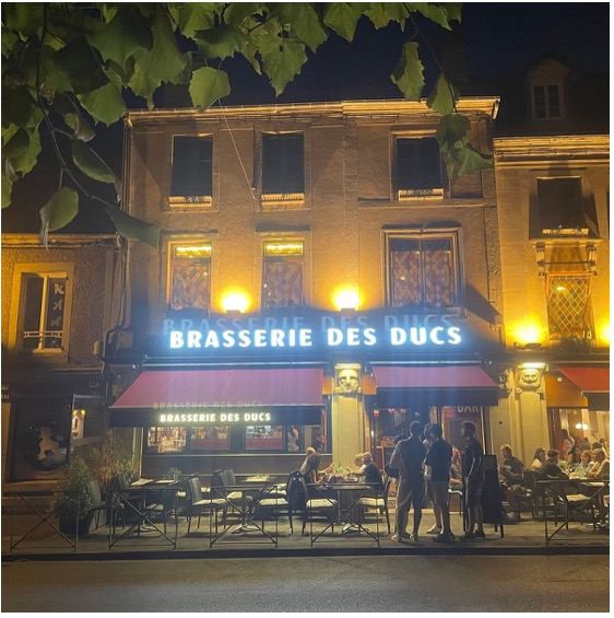 The Brasserie des Ducs lit up at night, with diners at tables outside
