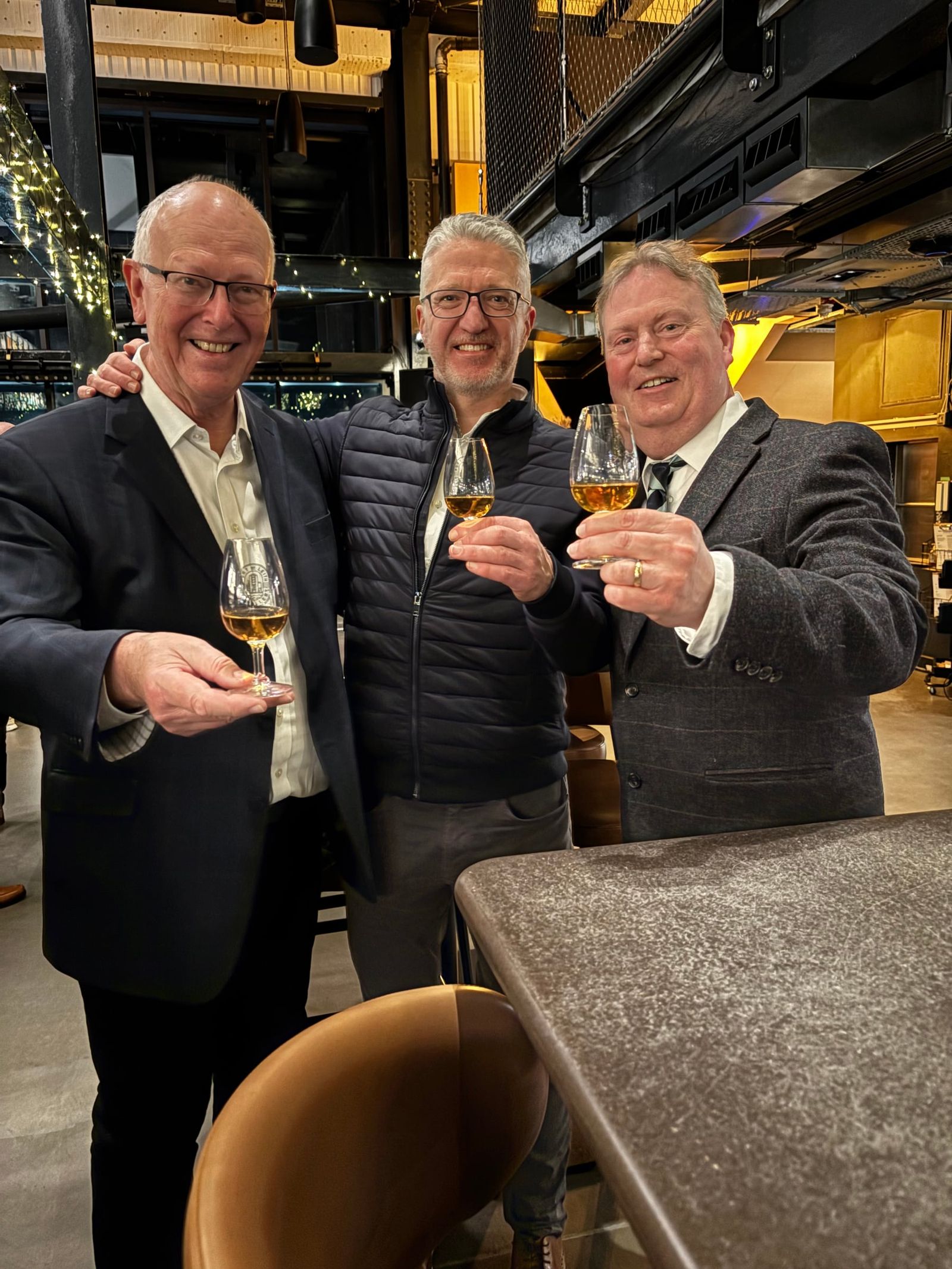 Three Distillers’ Company members raising glasses of whisky at a Port of Leith social.