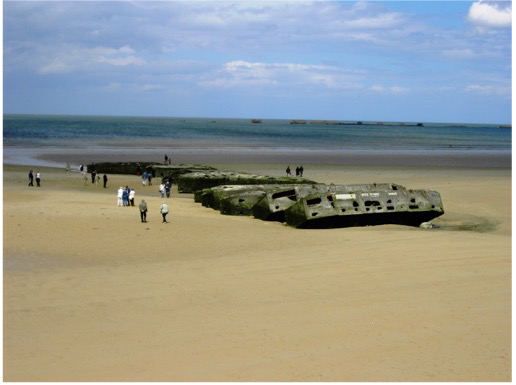 Concrete remains of the Mulberry harbour on the sand at Arromanches, with people walking beside them