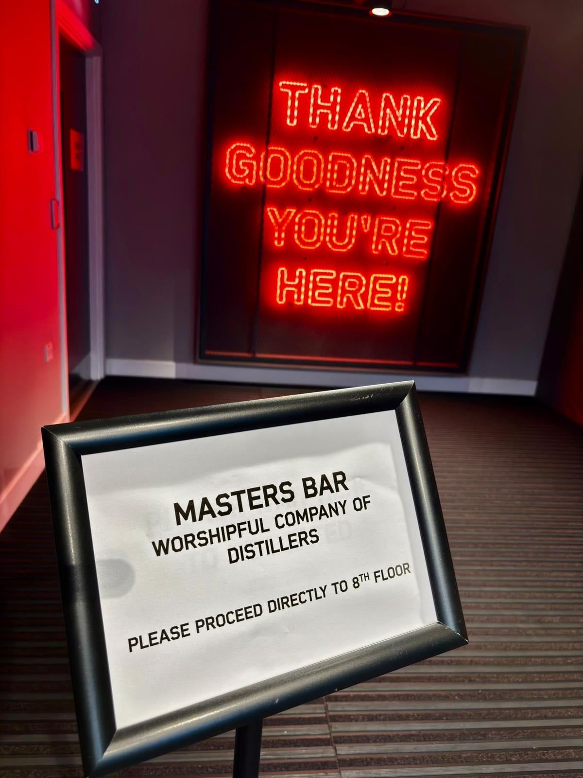 A sign for the Masters Bar of the Worshipful Company of Distillers beneath a neon welcome.