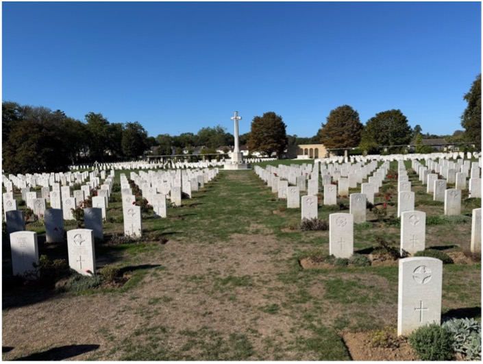 Rows of Commonwealth headstones at Ranville War Cemetery, with the Cross of Sacrifice beyond