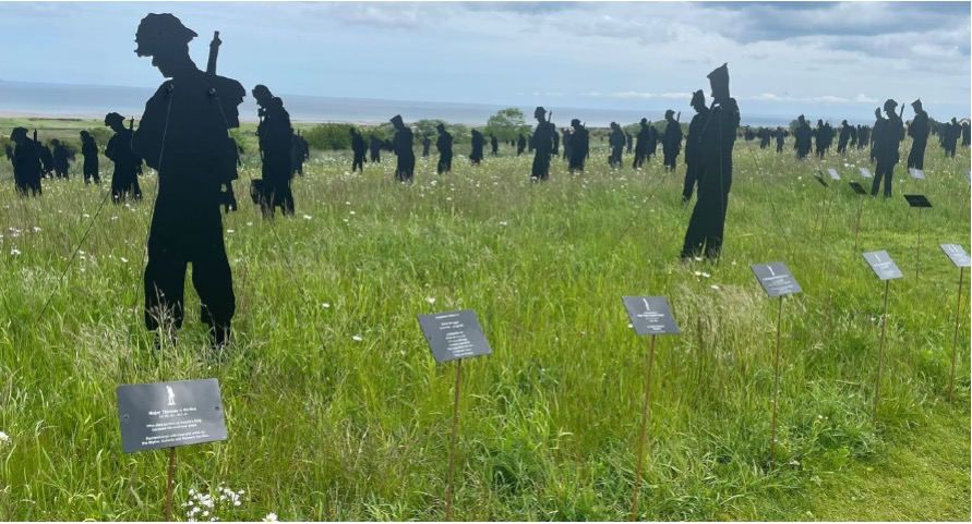 Silhouettes of soldiers and nurses standing in a meadow at the Standing with Giants installation, with name plaques in the grass