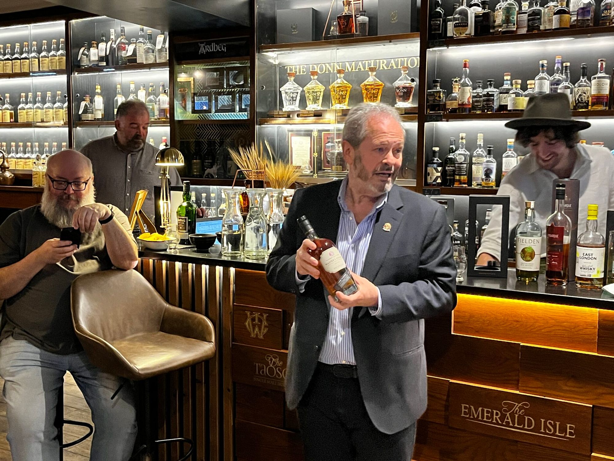 A man in a suit holding a whisky bottle at the bar of the Soho Whisky Club