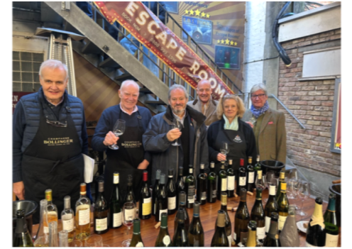 The Wine and Spirits Committee tasting, six people behind bottles under an Escape Room sign