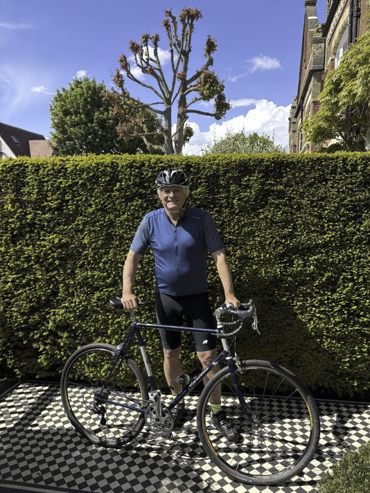 Nick Carr in cycling kit with a road bike, beside a hedge and a pollarded tree