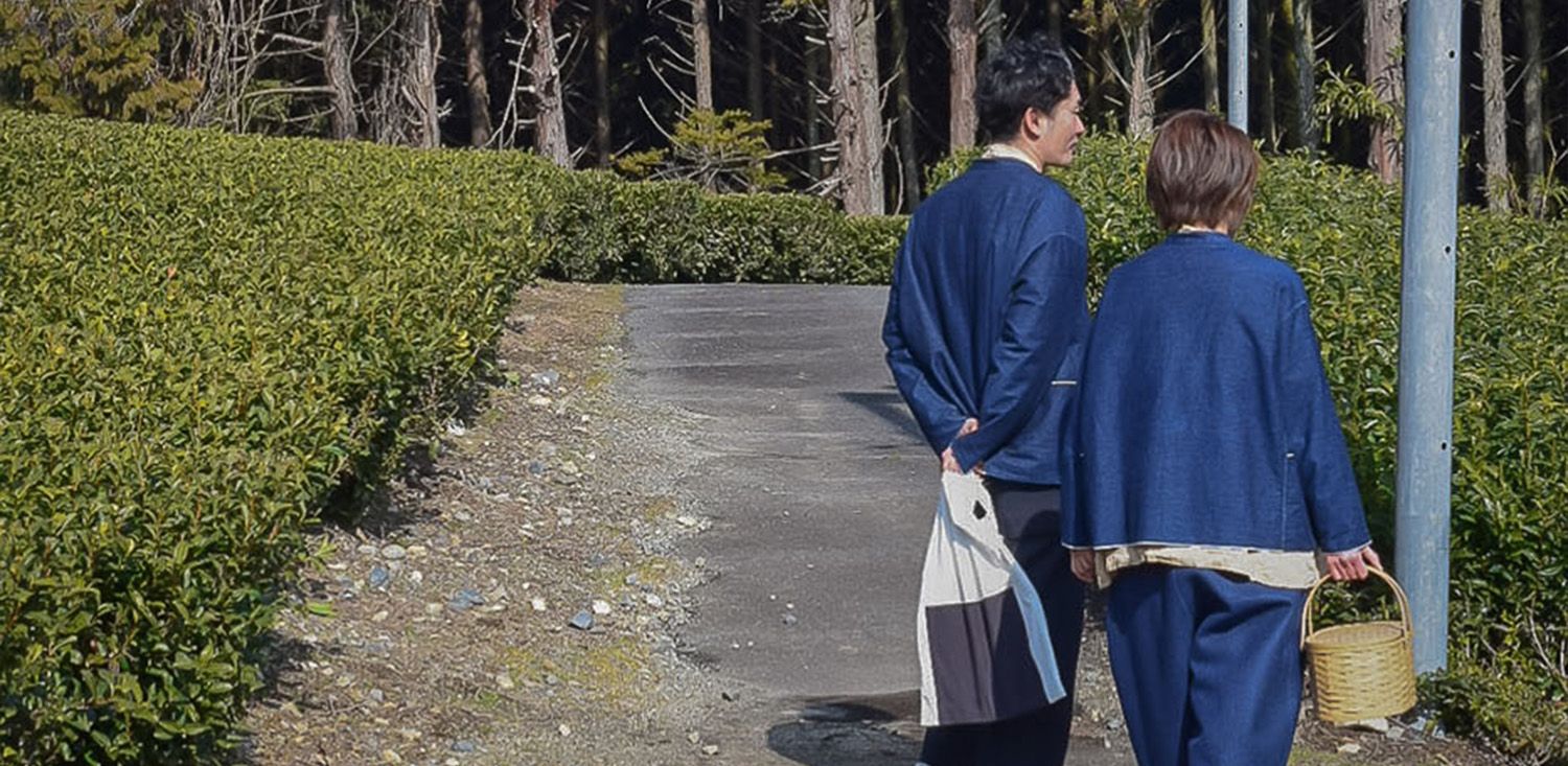 Two people in blue traditional outfits walking along a path with trees in the background